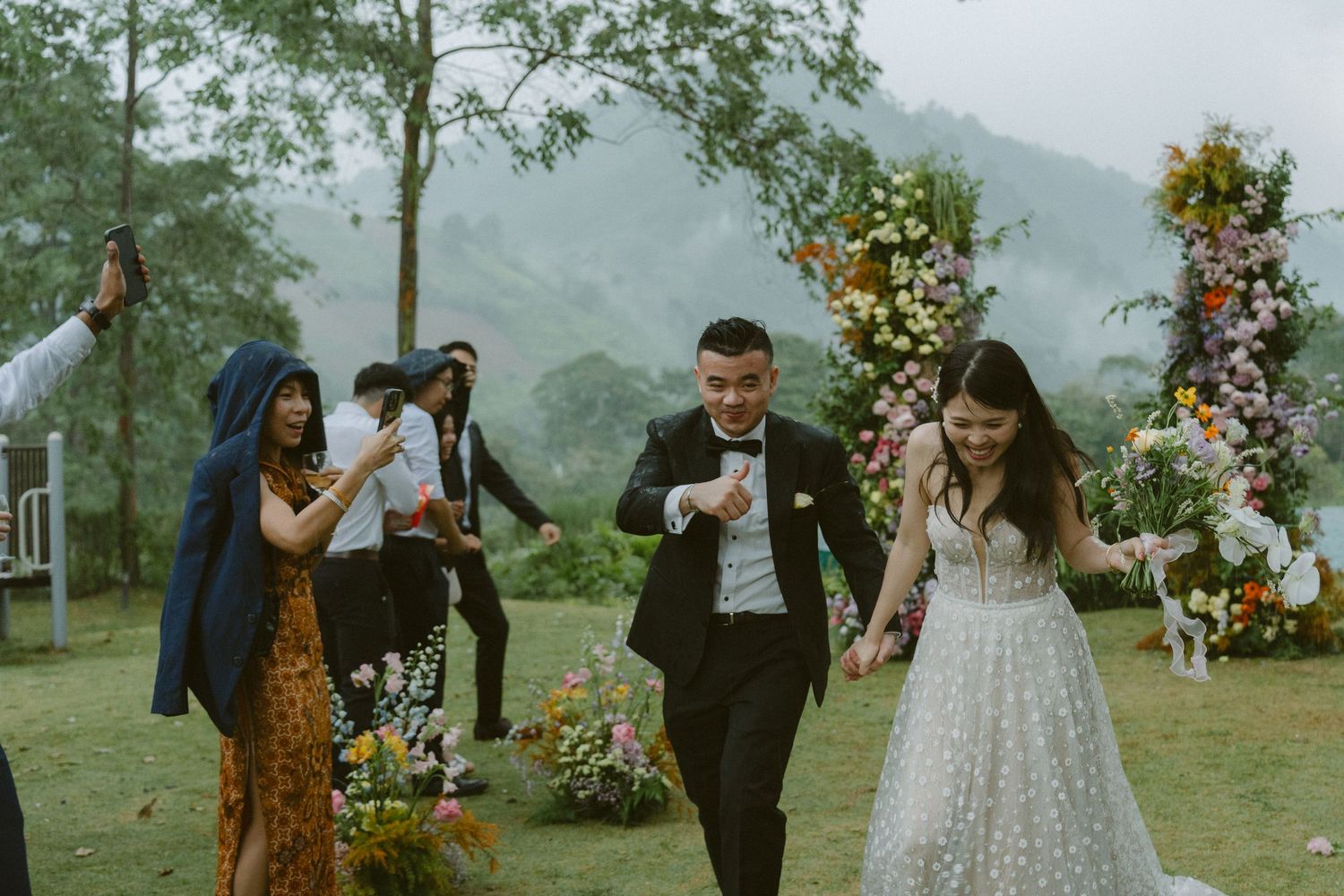 Joyful wedding celebration with guests dancing and celebrating outdoors against a scenic mountain backdrop.