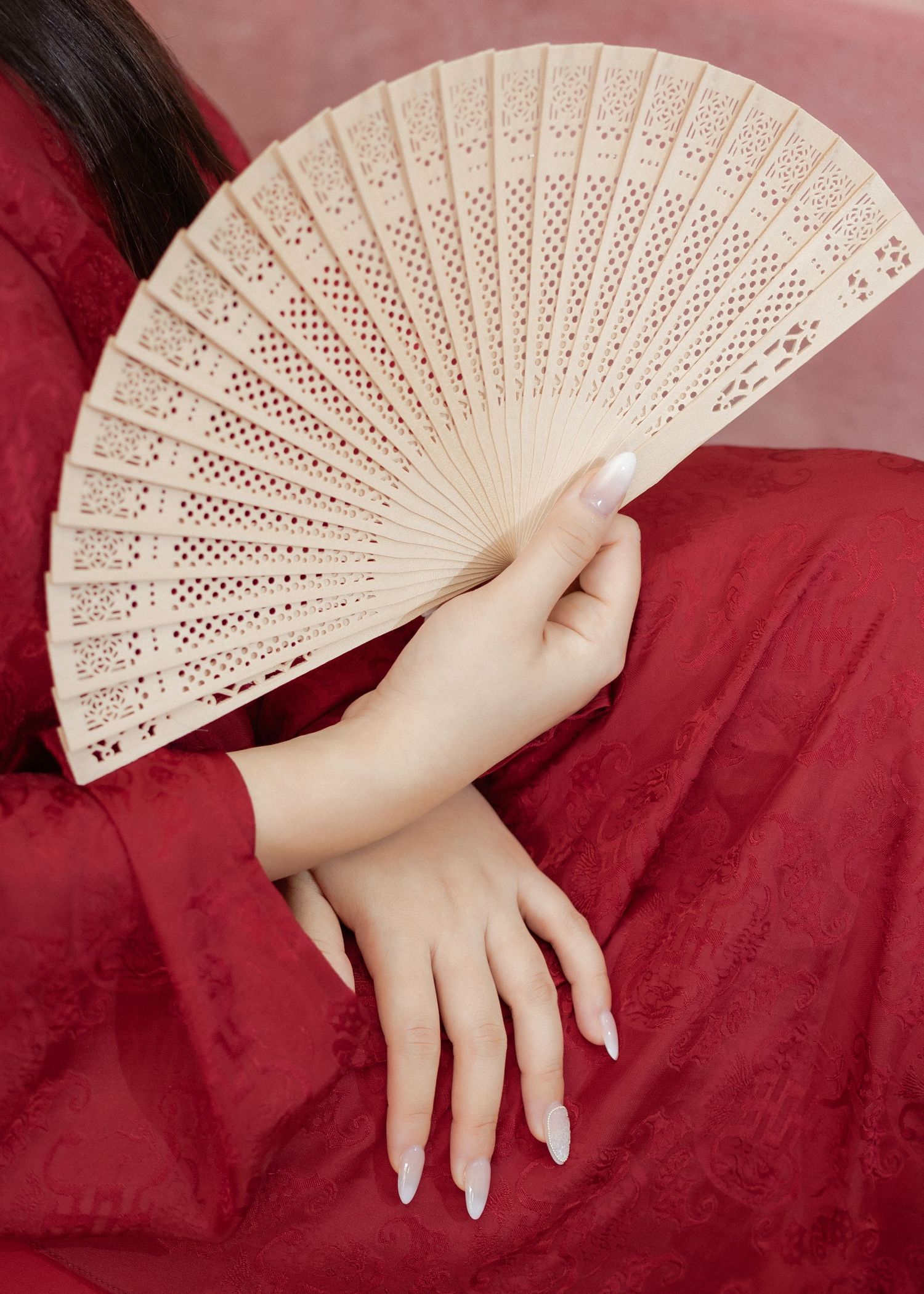 Delicate white folding fan held against a rich burgundy velvet backdrop with a hand showing polished nails.