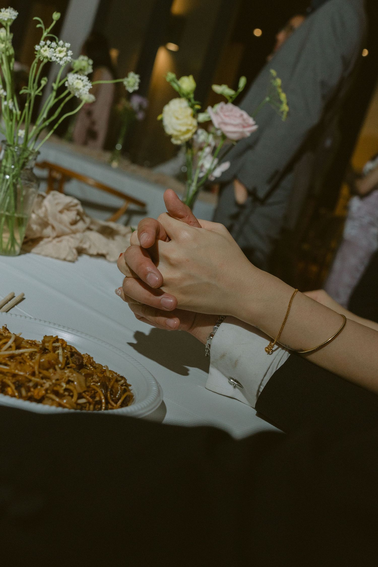 Elegant event setup with white flowers and hands writing notes on paper near a plate with golden-brown food.