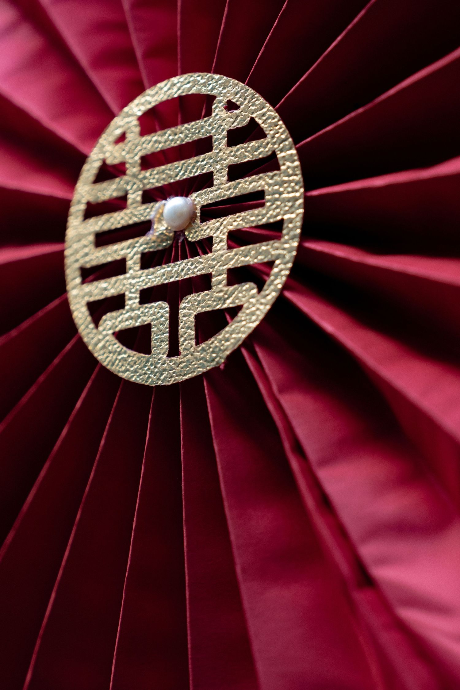 Gold Asian double happiness symbol decorative piece mounted on deep red pleated silk fabric background.