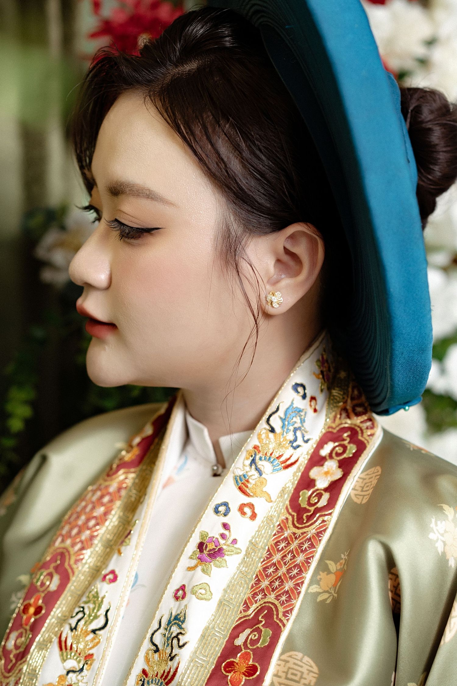 Portrait of someone wearing a turquoise beret and traditional Asian robe with ornate embroidered details.