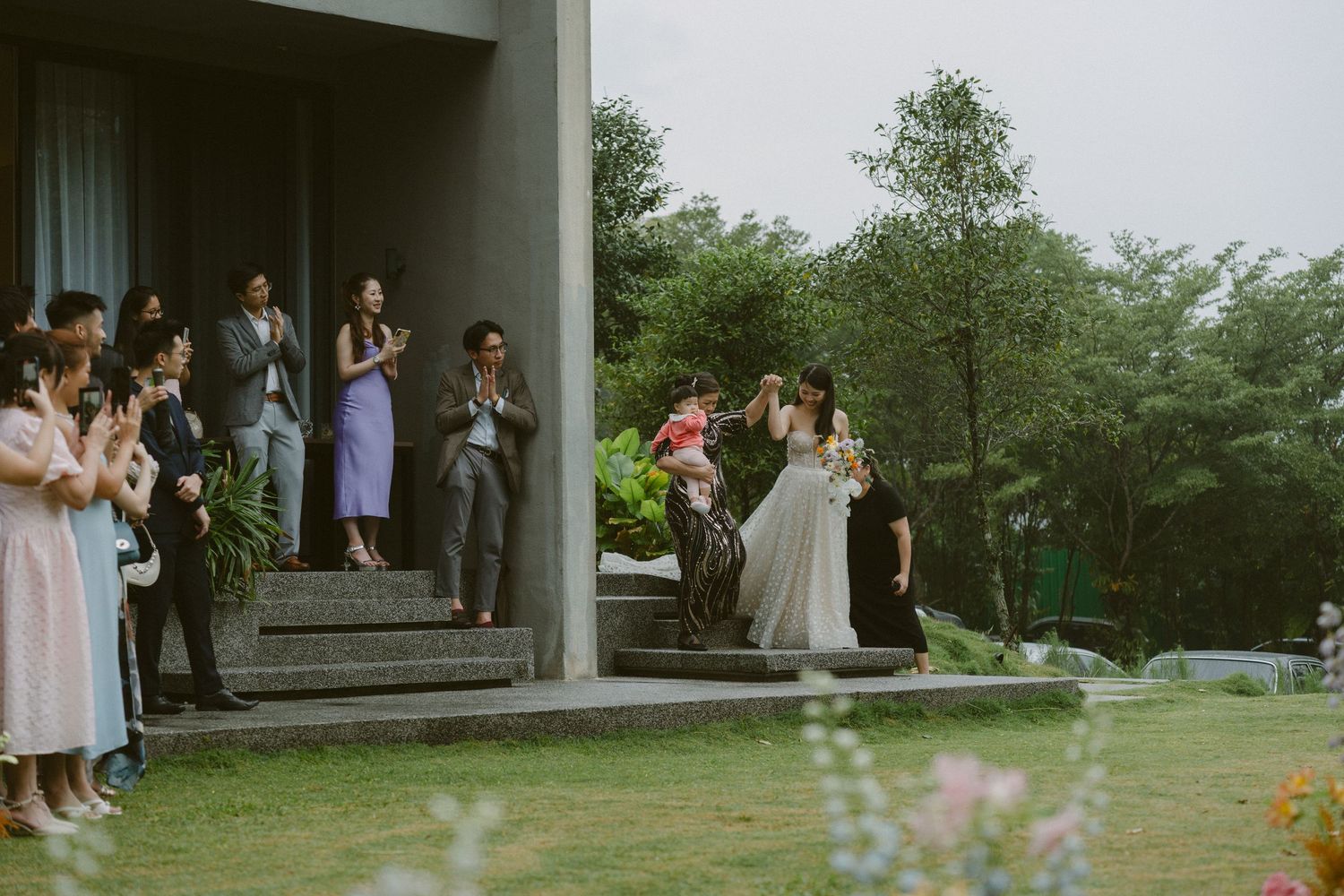 Outdoor wedding ceremony setup with rustic wooden structure and gathered guests in a garden setting.