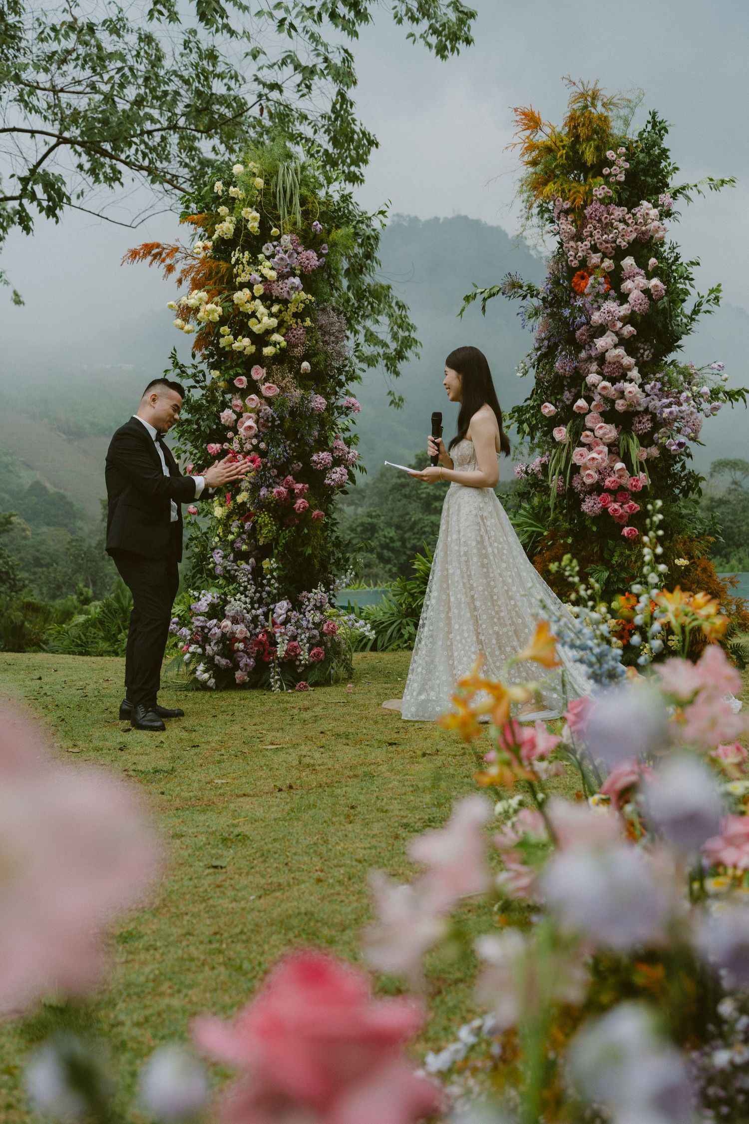 A romantic outdoor wedding ceremony set against misty mountains with beautiful floral arrangements framing the scene.