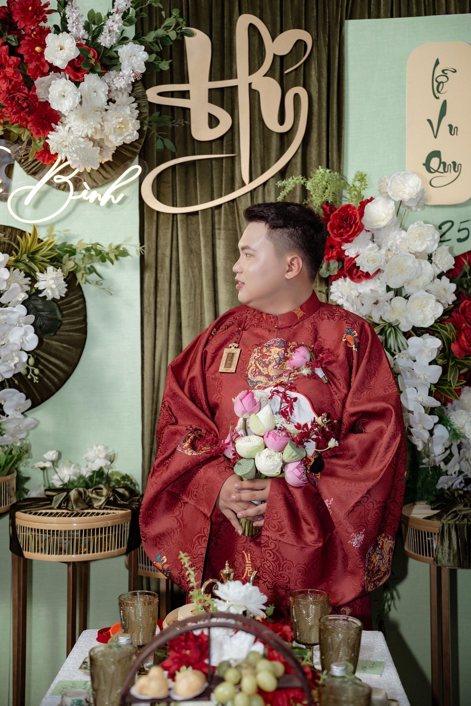 Traditional Vietnamese wedding ceremony setup with red silk ao dai, floral decorations and elegant gold calligraphy backdrop.