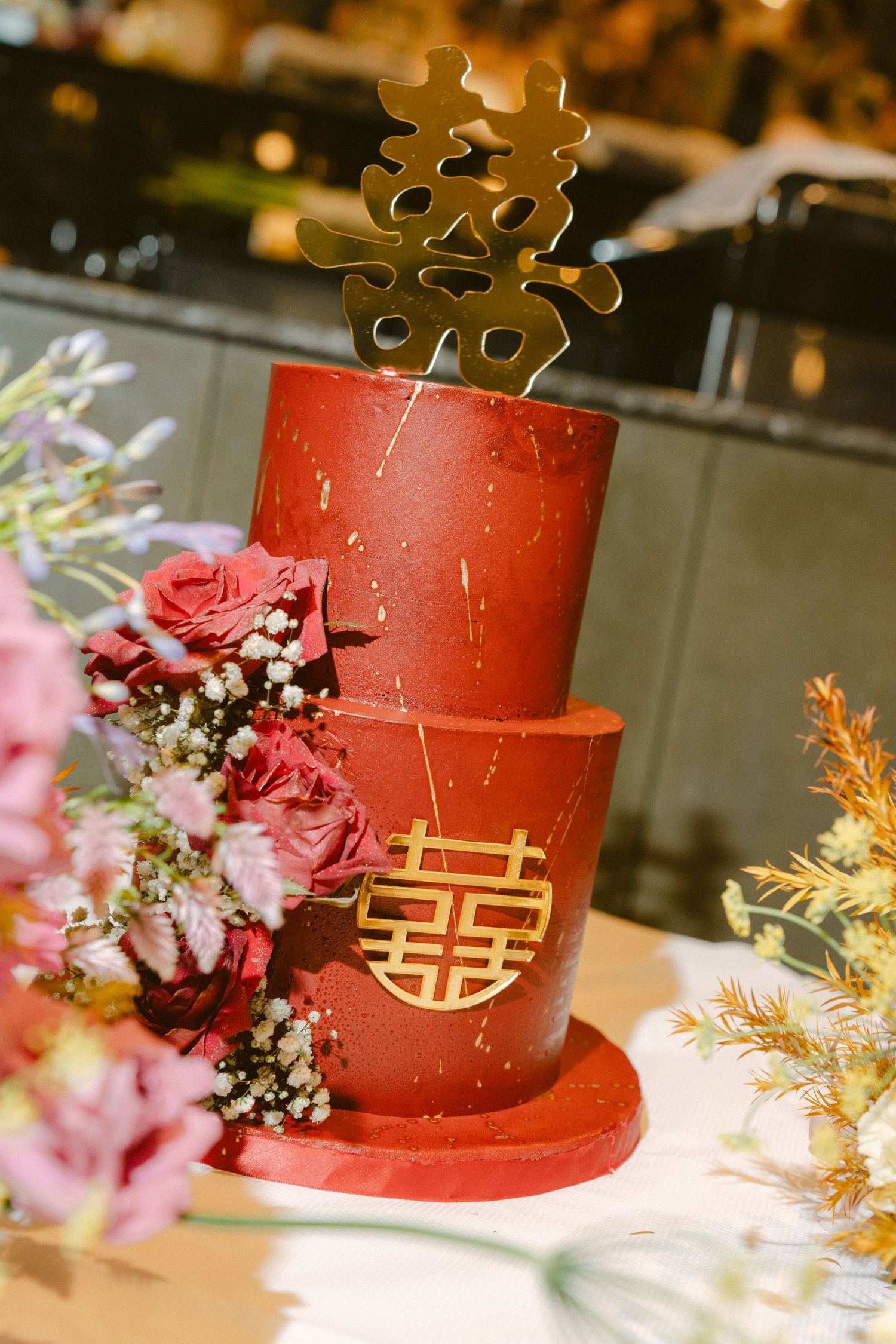 Red and gold traditional Chinese wedding cake decorated with Double Happiness symbol and roses in an elegant setting.