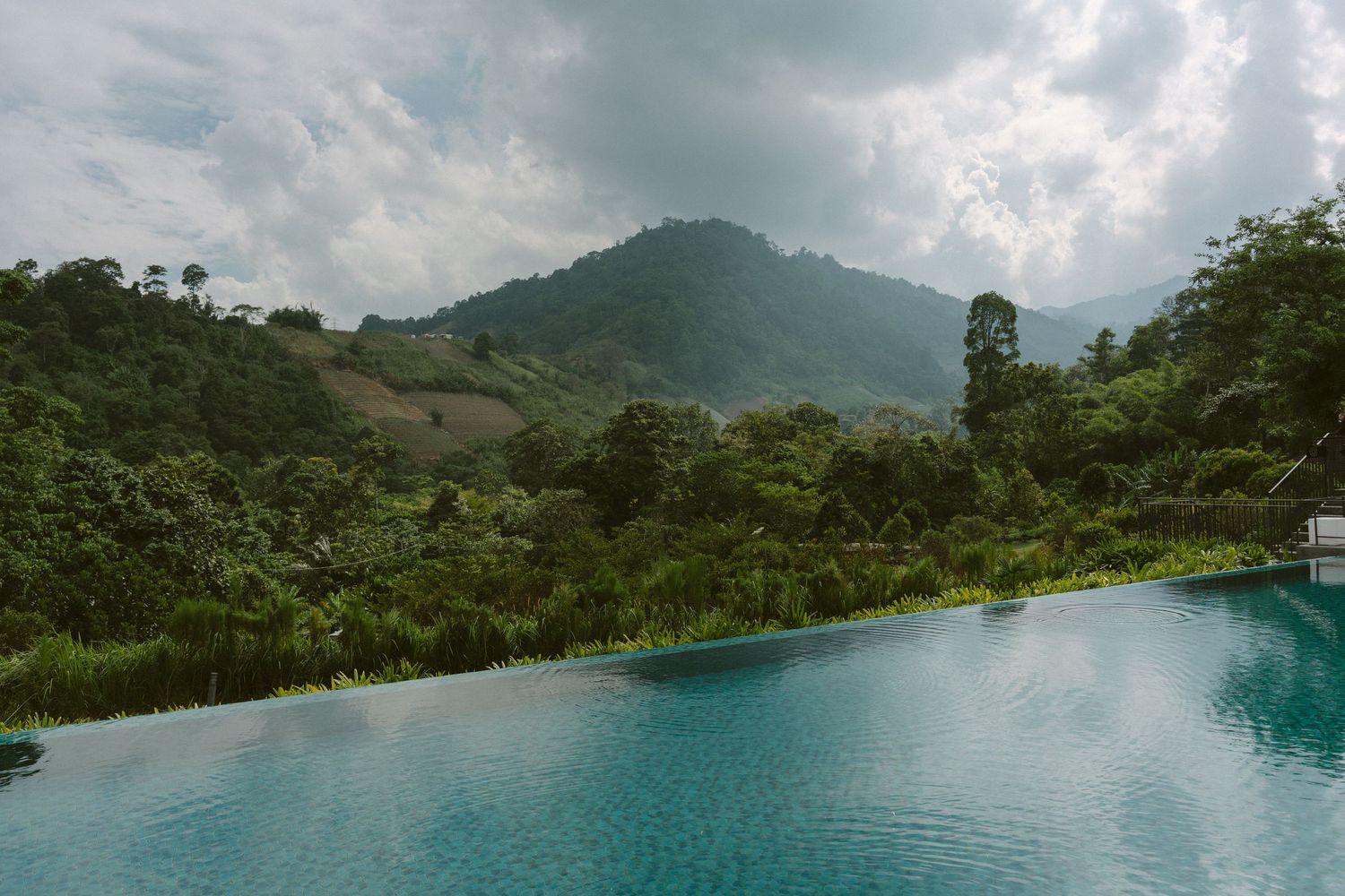 Mountain lake with infinity pool edge overlooking lush green tropical landscape and cloudy sky in Costa Rica.