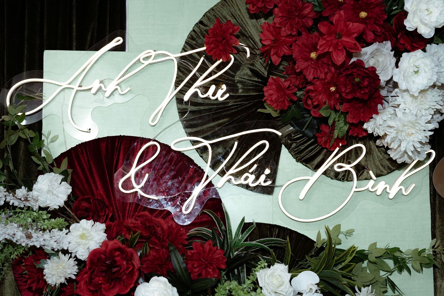Elegant wedding sign surrounded by vibrant red and white floral arrangements with greenery on mint green background.