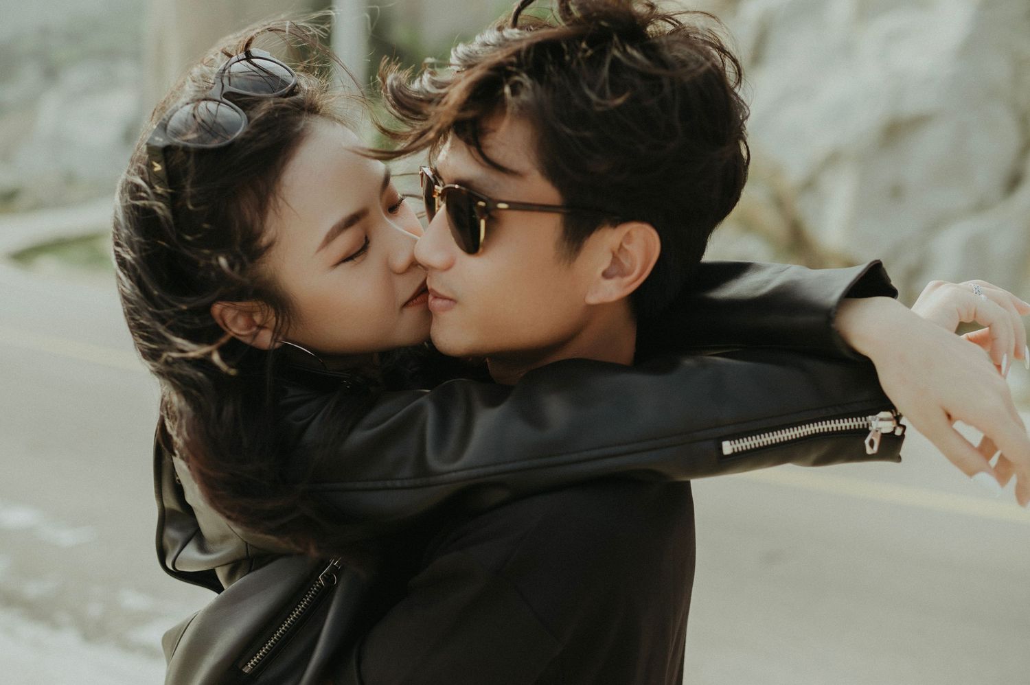 A romantic couple in leather jackets sharing an intimate kiss while embracing outdoors.