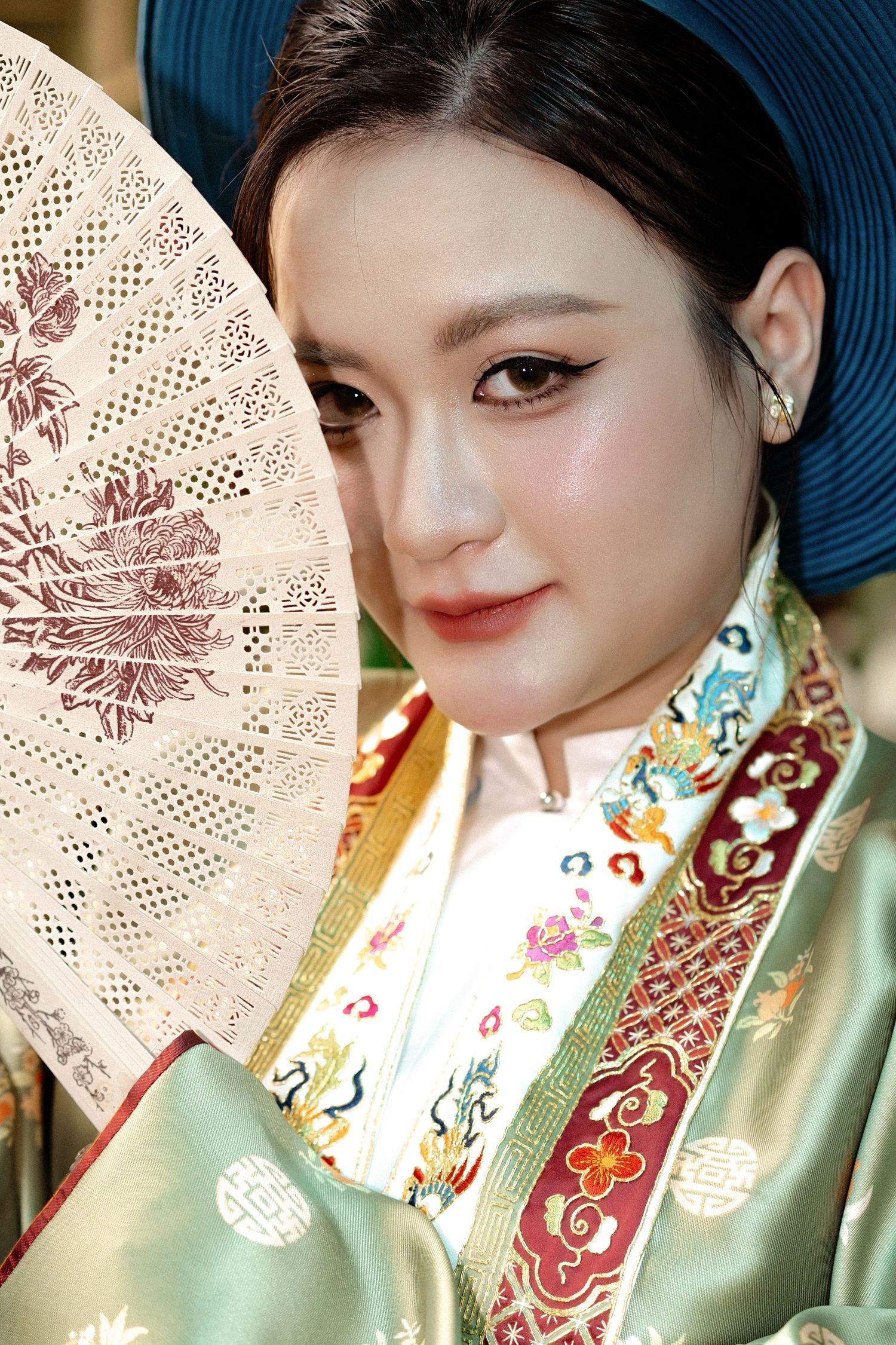 Traditional Chinese attire with mint green silk and embroidery is paired with a decorative lace fan and navy blue sun hat.