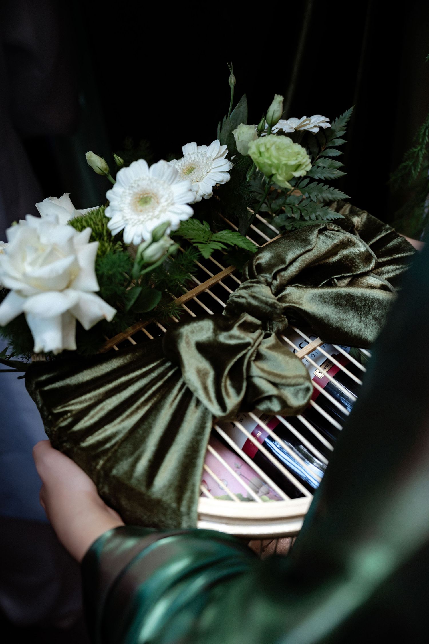 White gerbera daisies and roses arranged with green velvet bow on piano keys in moody lighting.