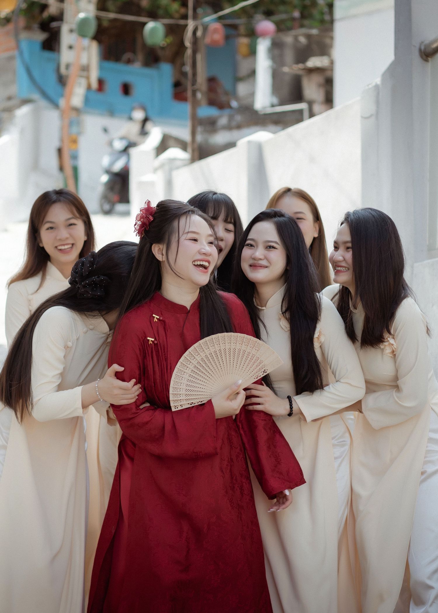 A group in traditional Asian attire shares a joyful moment together, with one person in red holding a folding fan.