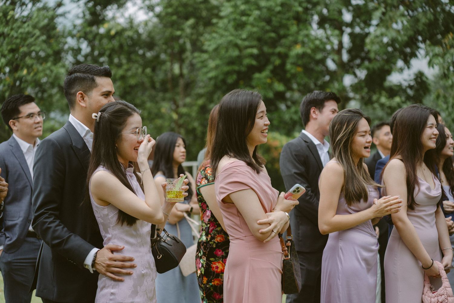 Guests mingle and socialize at an outdoor wedding celebration with lush greenery in the background.