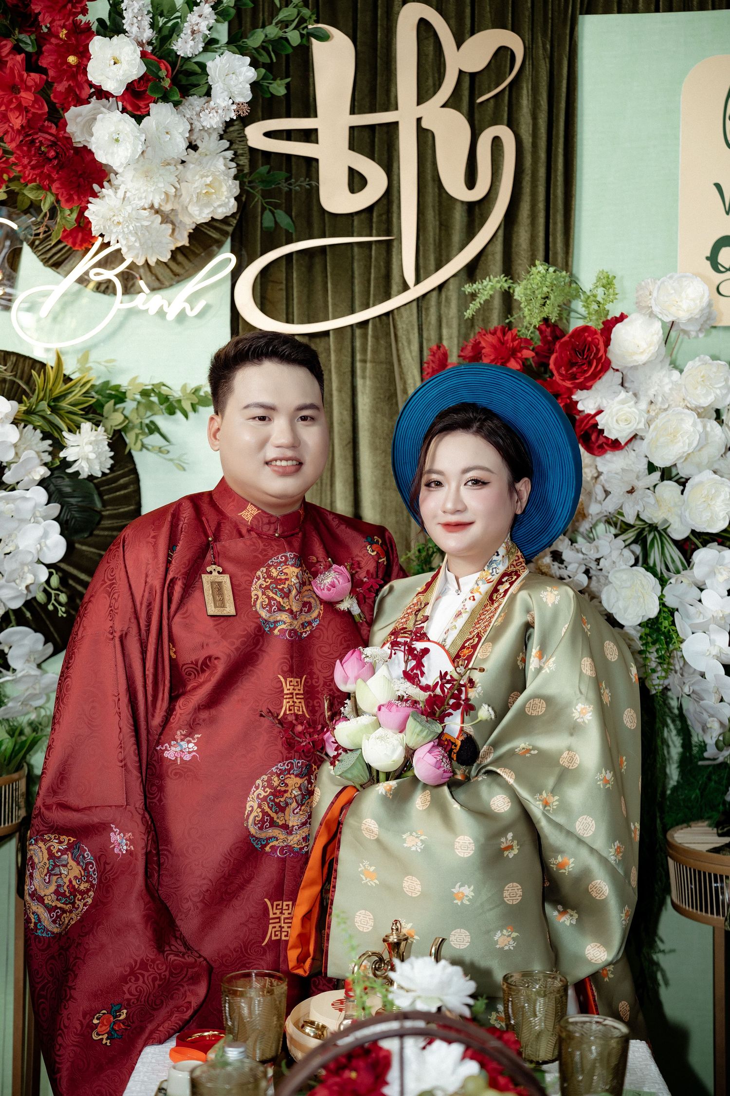 A traditional Vietnamese wedding ceremony setup with red and gold attire, blue headpiece, and elegant floral decorations.