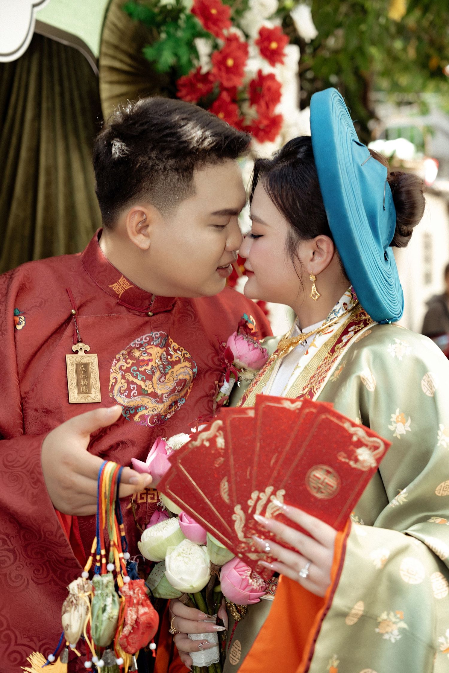 A couple in traditional Chinese wedding attire share a romantic moment while holding red envelopes and wearing festive clothing.