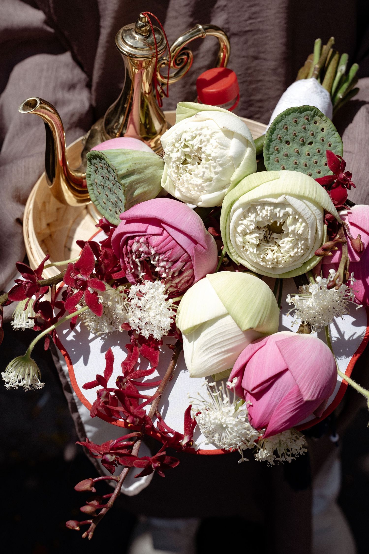 Elegant bouquet of pink and white ranunculus flowers with a decorative gold teapot against a dark background.