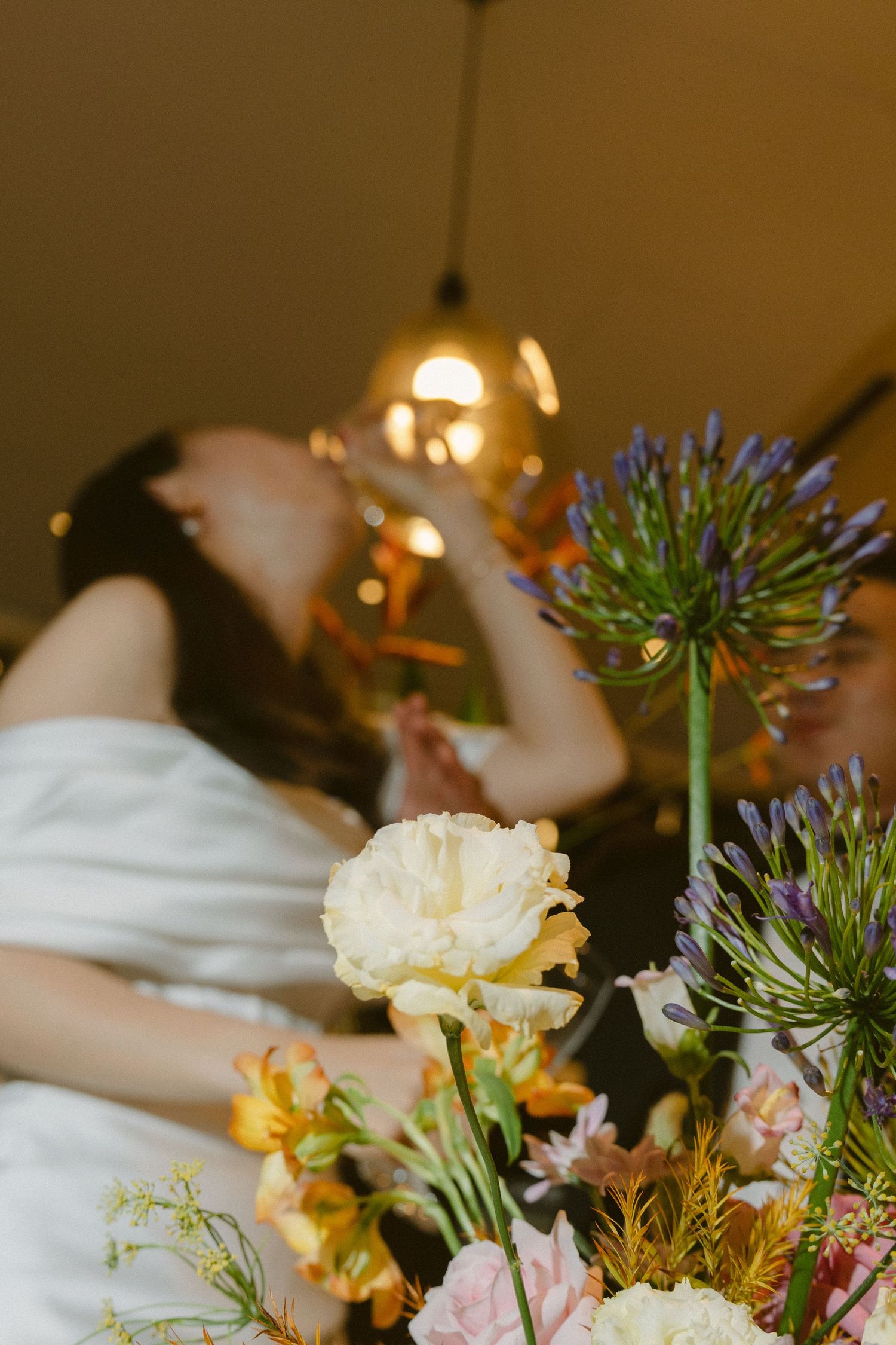 Close-up of romantic floral arrangement with delicate blooms and greenery against warm ambient lighting.