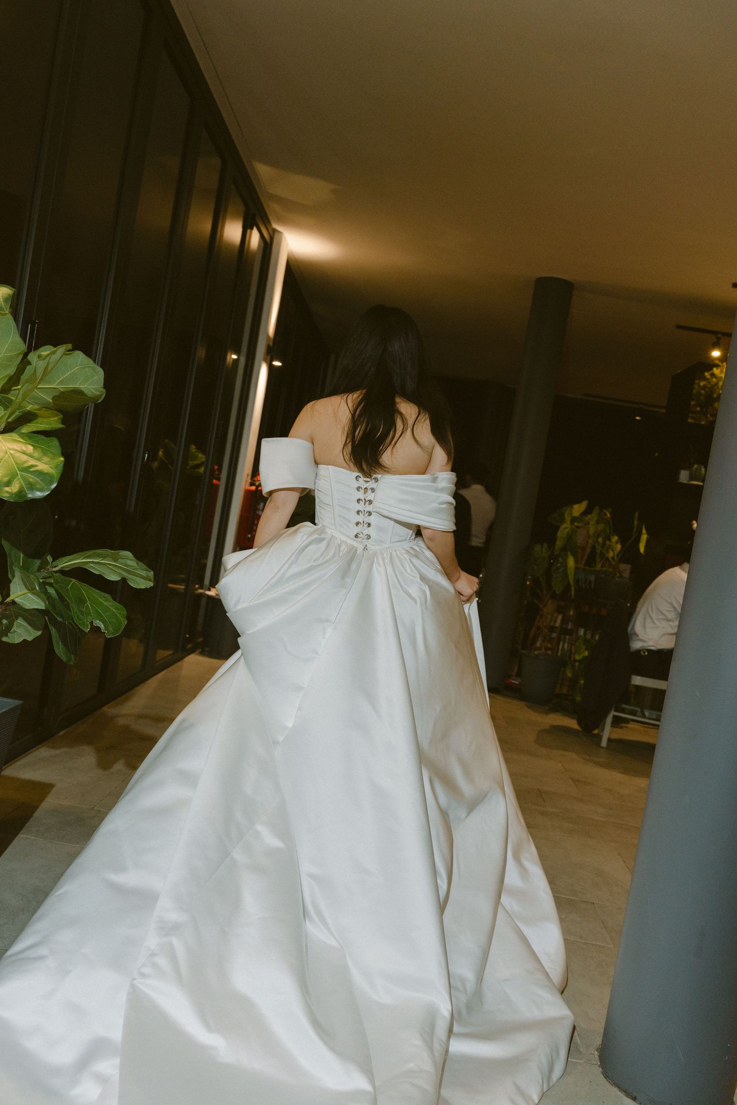 A person wearing a flowing white wedding gown spins around in an indoor setting creating elegant movement in the fabric.
