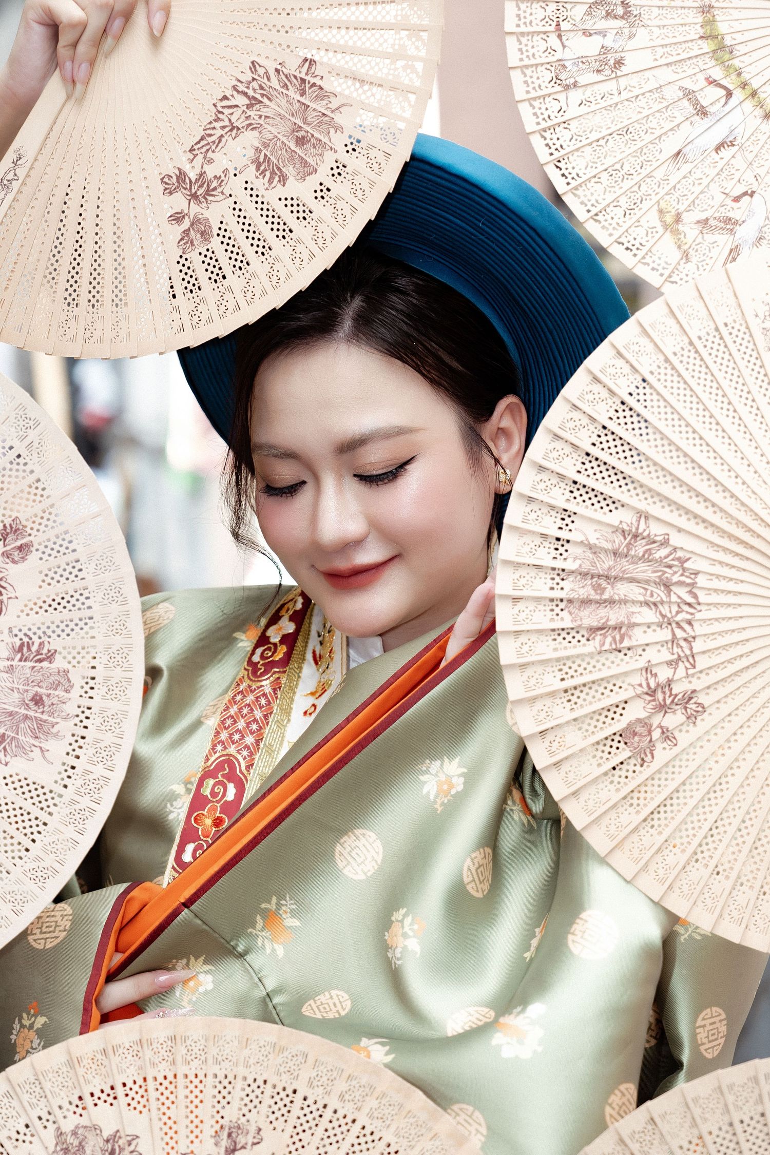 A person in traditional mint green hanfu holding delicate paper fans with floral patterns in soft lighting.