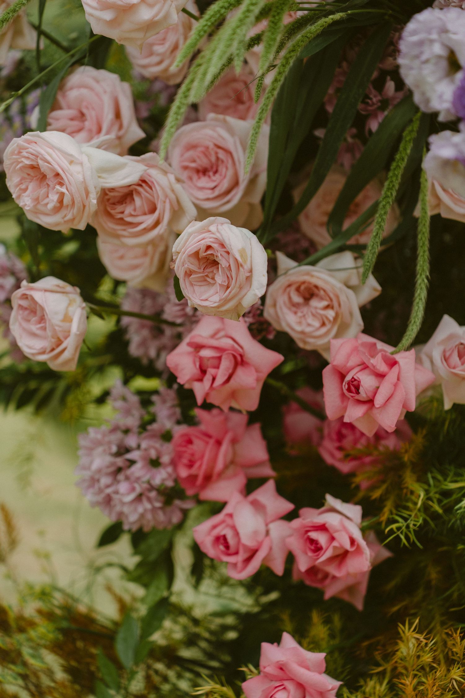 An elegant floral arrangement featuring pink and blush garden roses with delicate ferns and greenery against a soft background.
