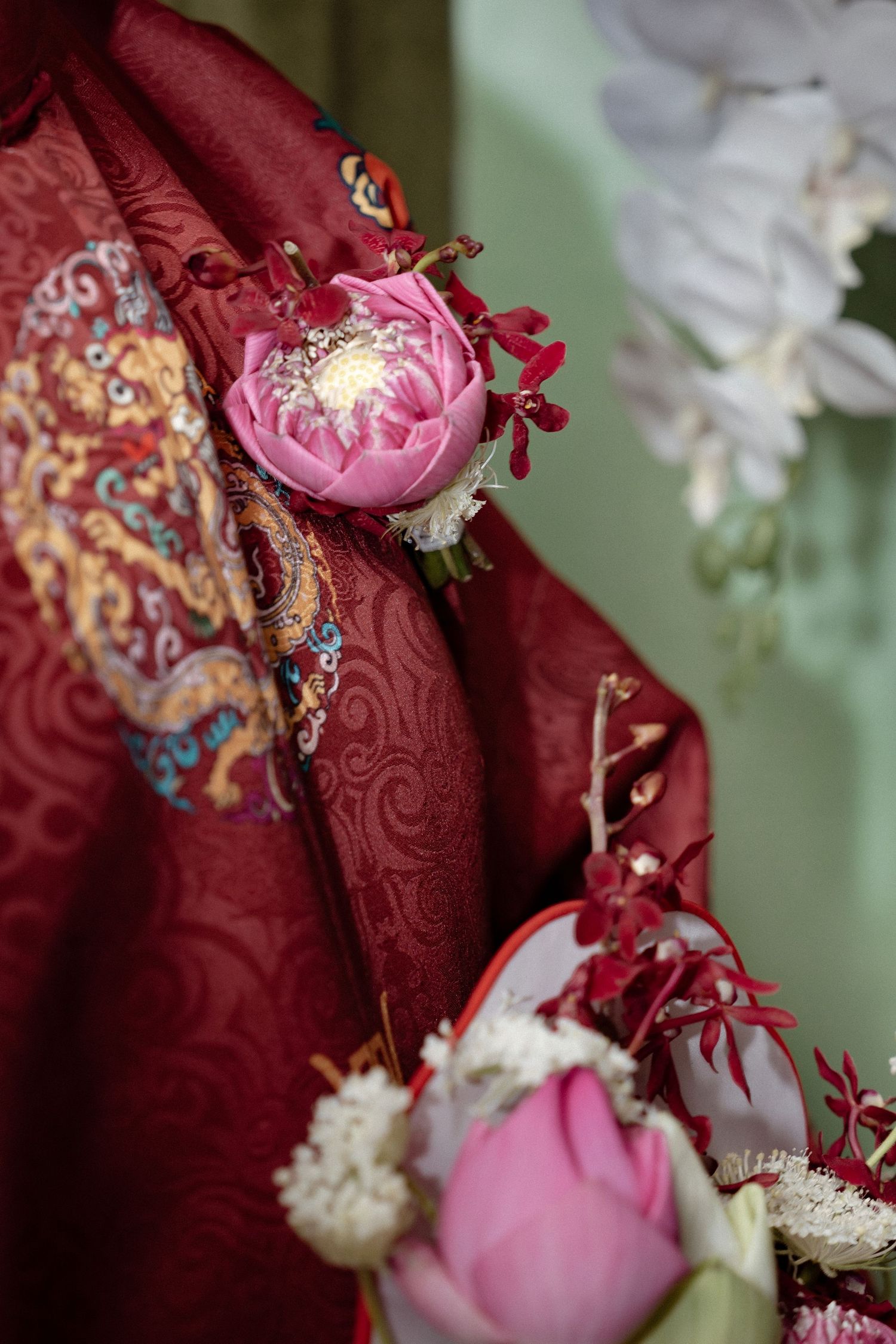 Pink peonies and flowers adorn a richly textured red fabric with ornate embroidered patterns.