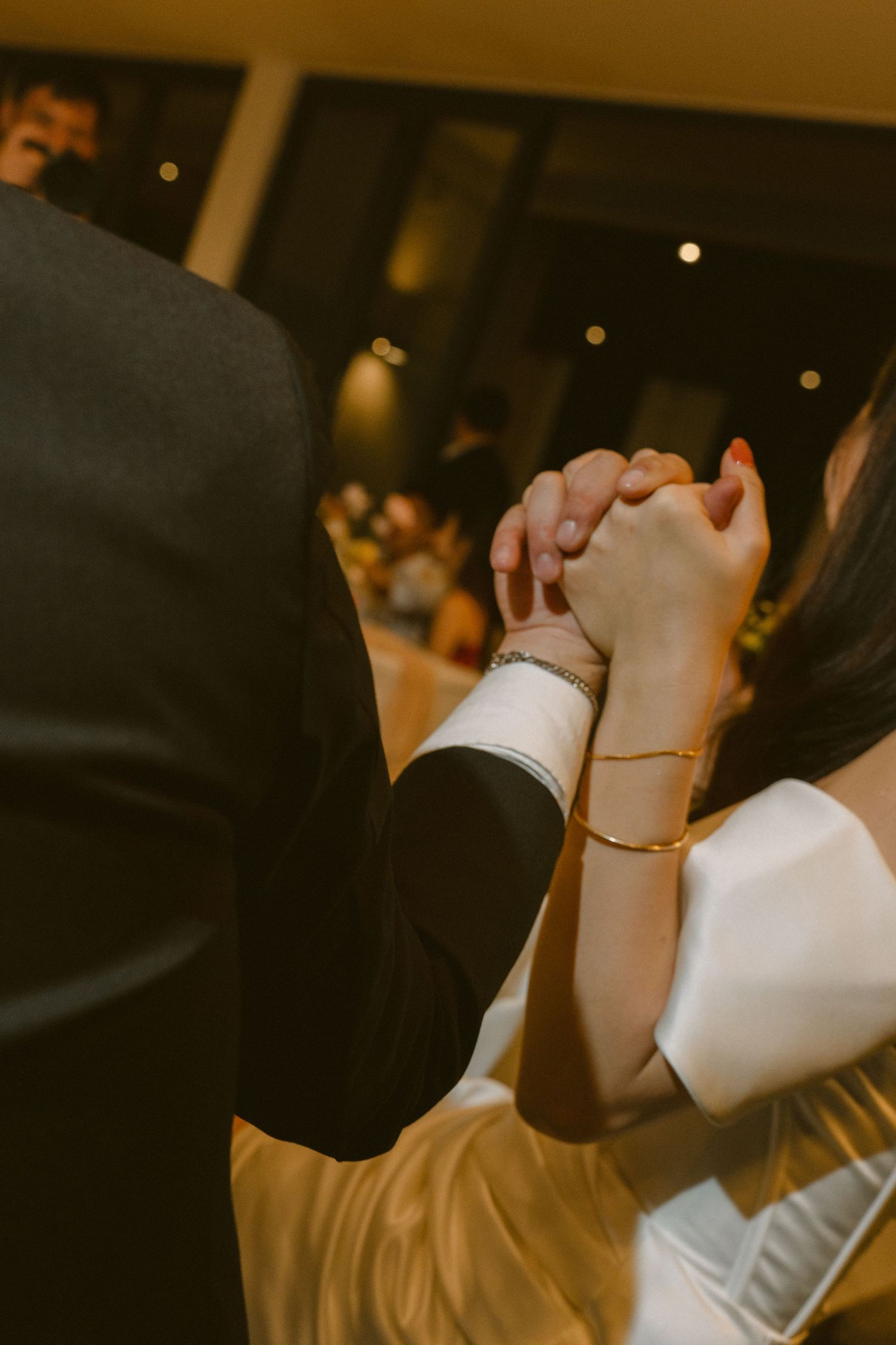 A close-up shot of hands clasped together during a wedding dance, with a white sleeve and black suit jacket visible.