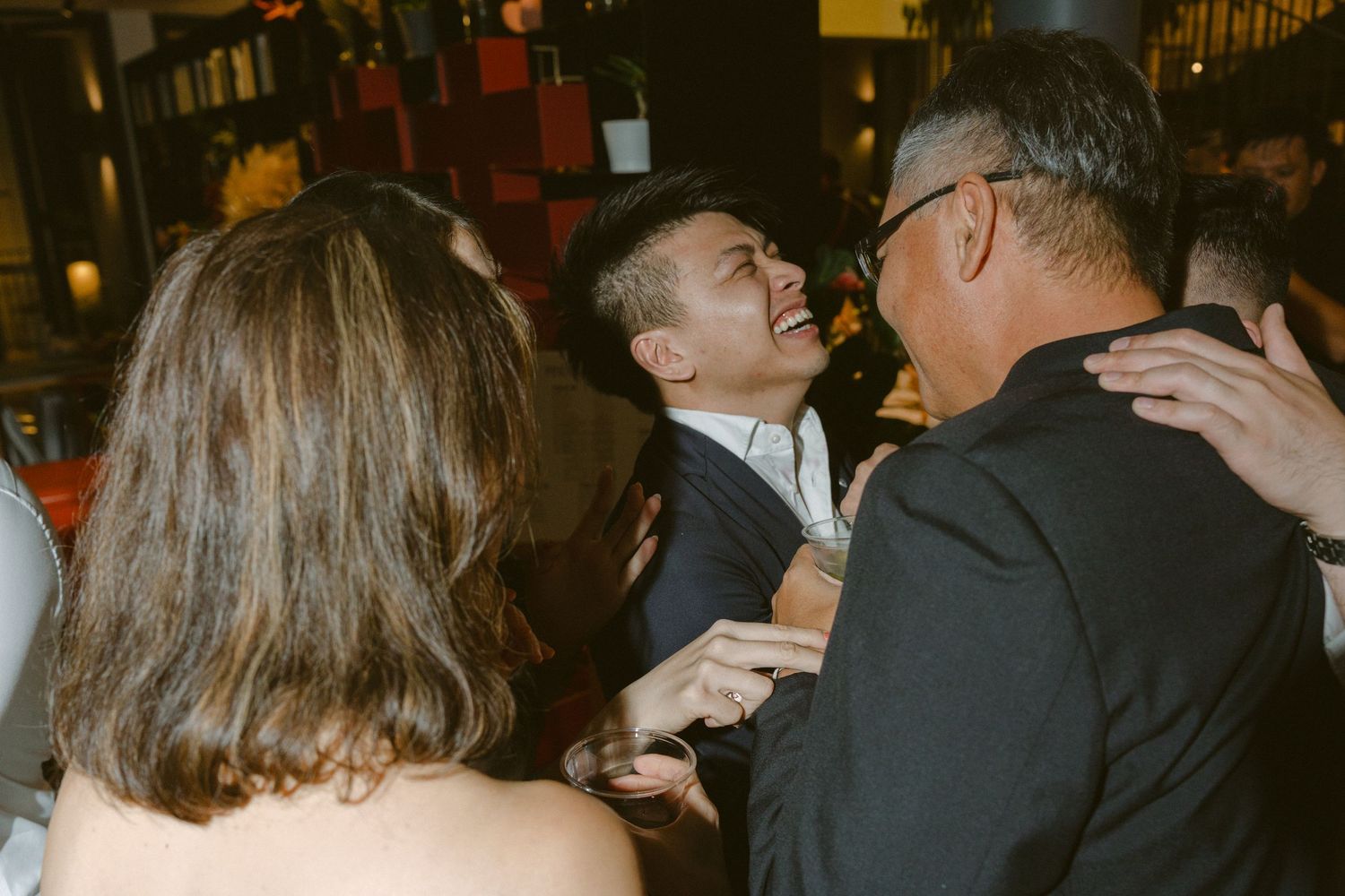 A crowd of people in formal attire mingle at an indoor social event or reception.
