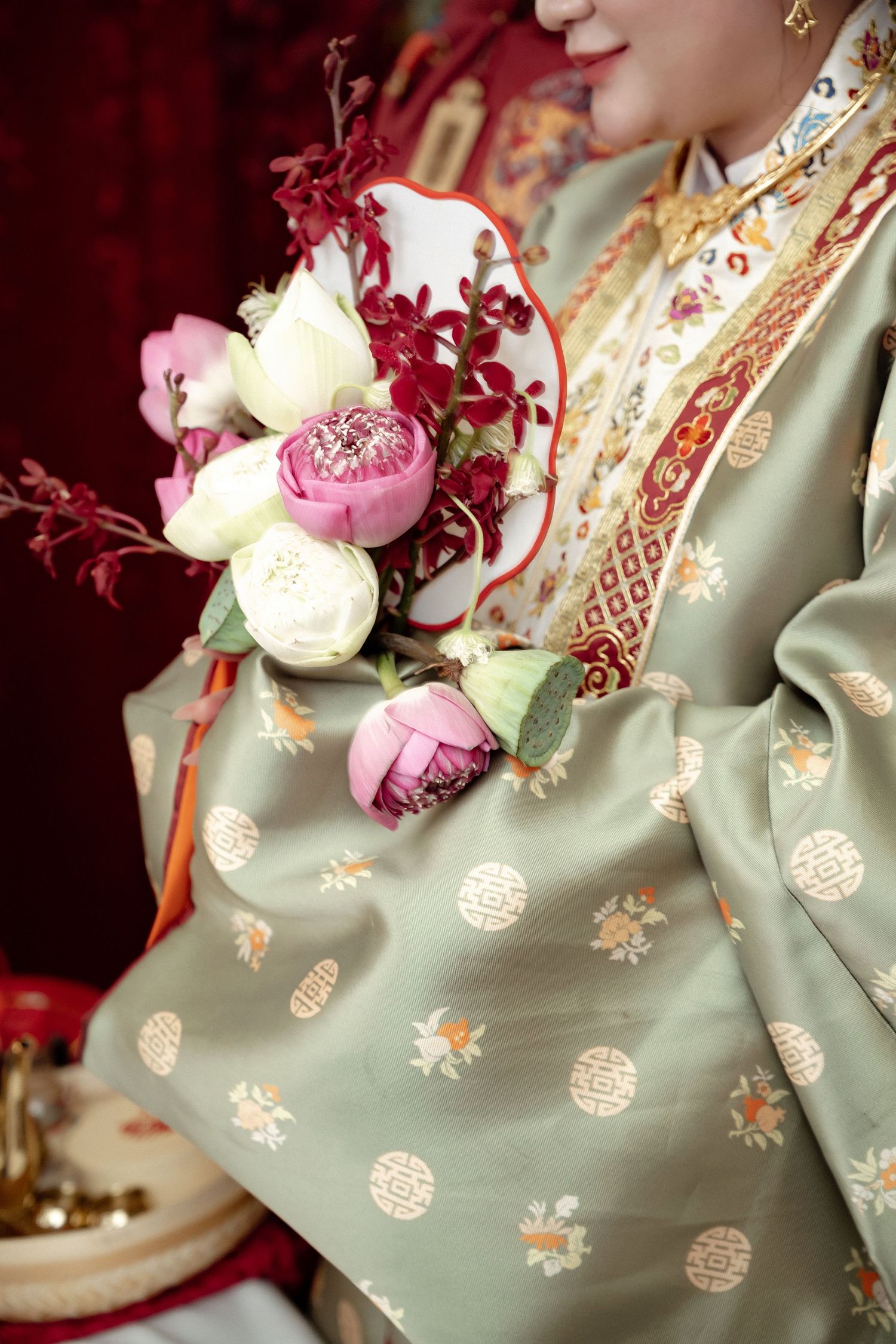 Beautiful floral arrangement of pink peonies and red branches held against sage green traditional Asian robe with gold motifs.