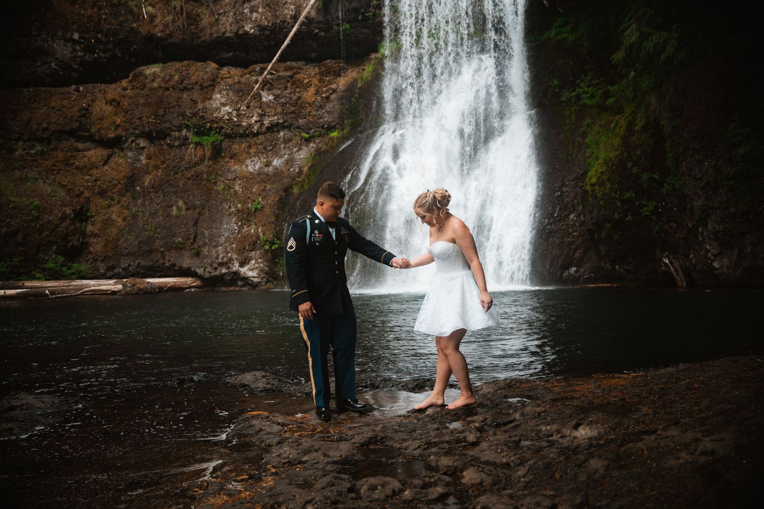 Waterfall creates dramatic backdrop for wedding portraits in Pacific Northwest forest setting.