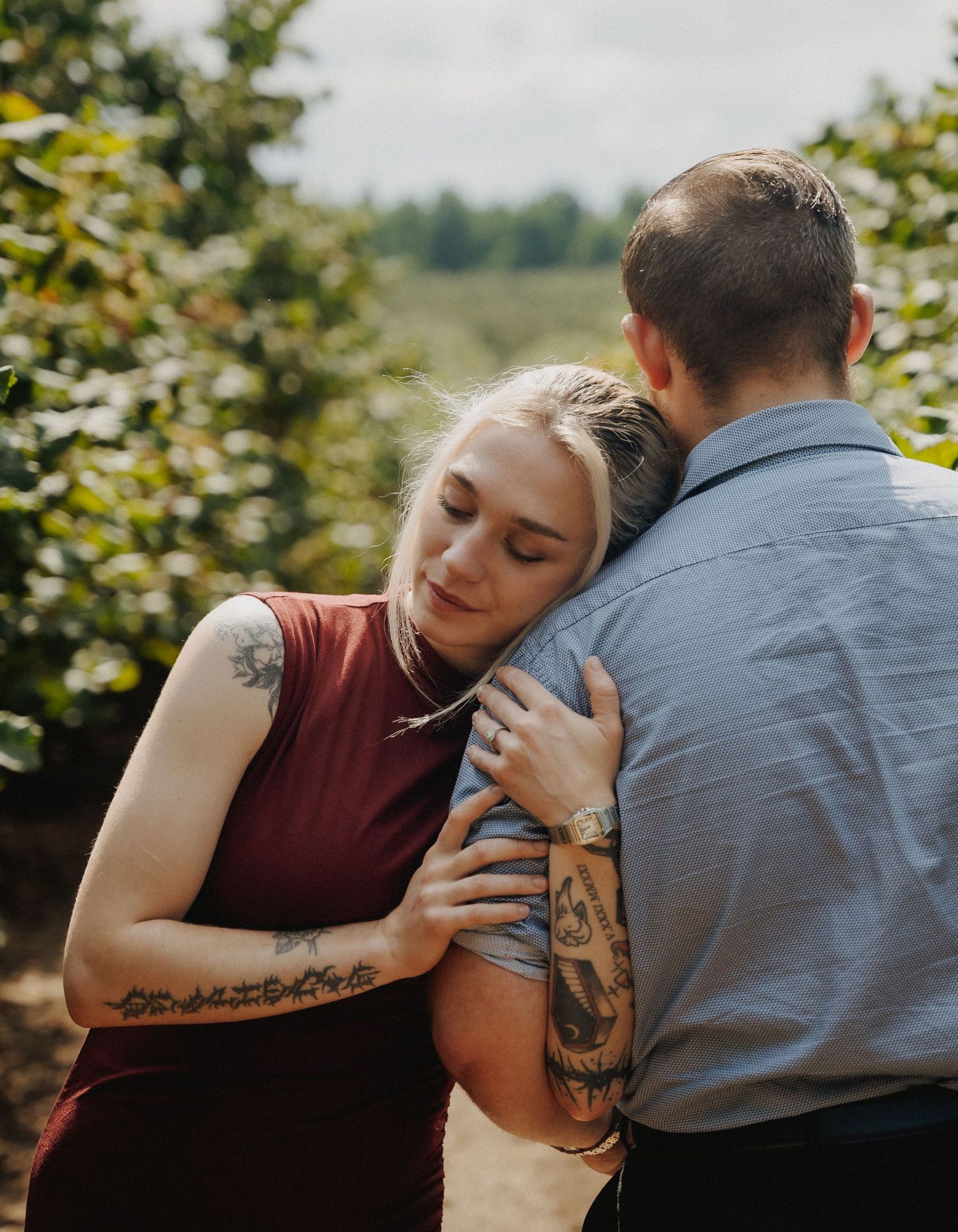 An intimate moment captured in an orchard showing tattoos and embraces.
