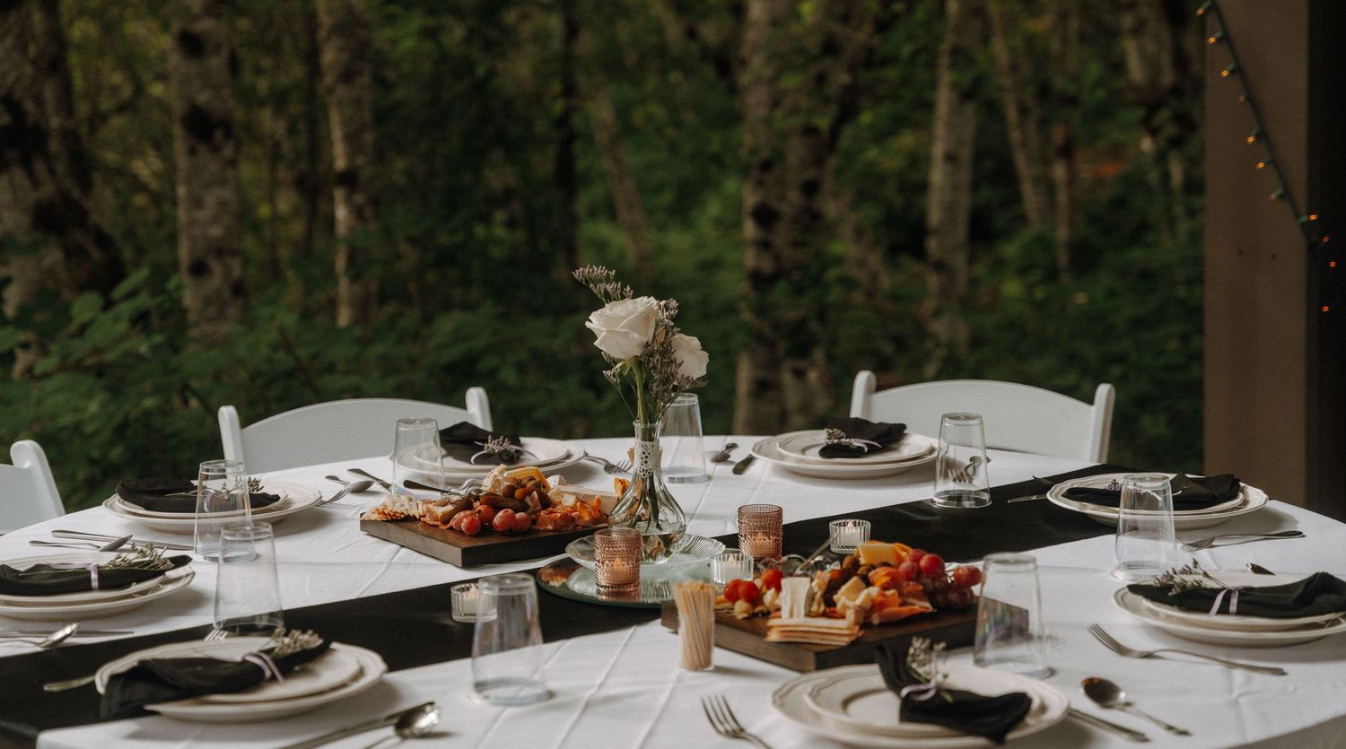 Elegant table settings at an outdoor wedding reception with forest backdrop.