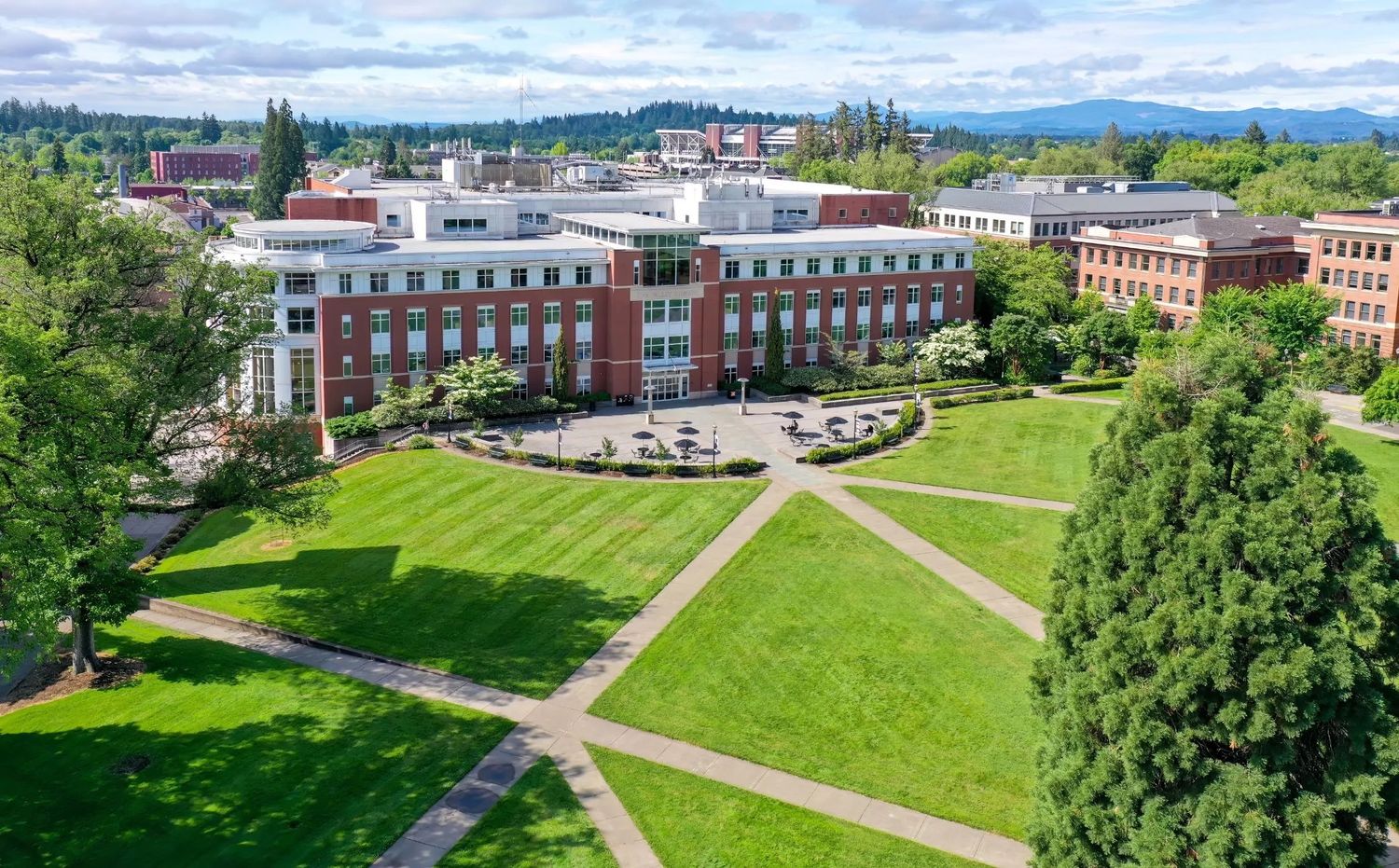 Aerial view of a sprawling university campus with red brick buildings, green lawns, and pathways surrounded by trees.