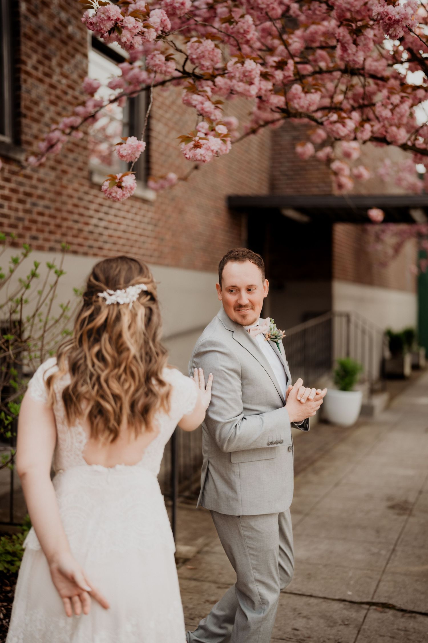 Spring wedding portraits with blooming cherry blossoms and brick building backdrop.
