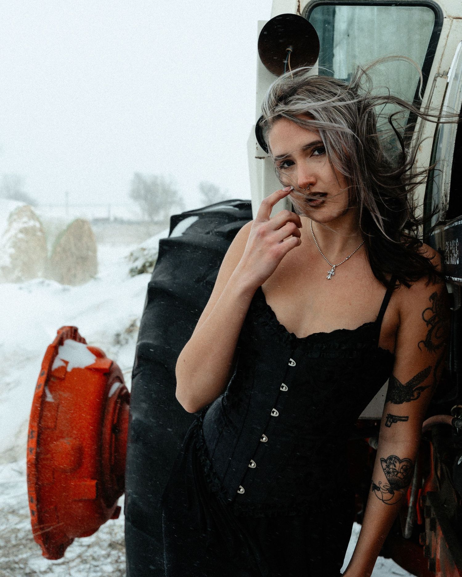 Gothic fashion model poses in black corset against snowy background with red canister visible.