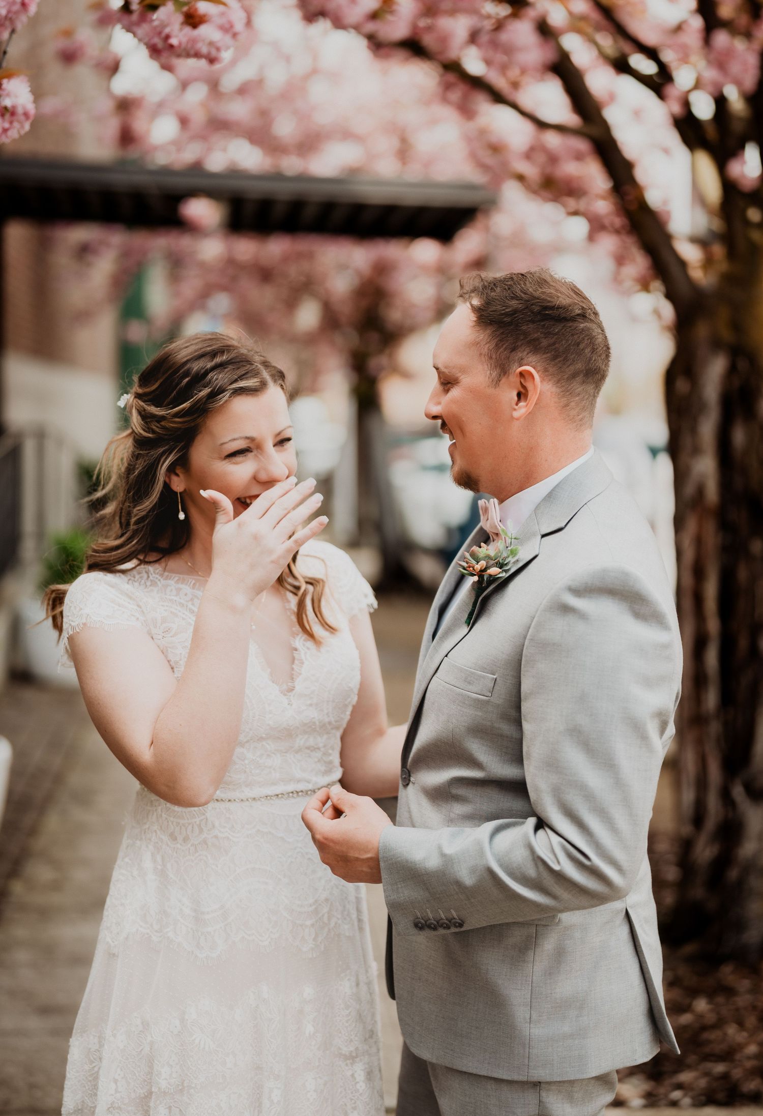 Intimate wedding portraits under beautiful pink cherry blossoms with a couple in grey and white attire.