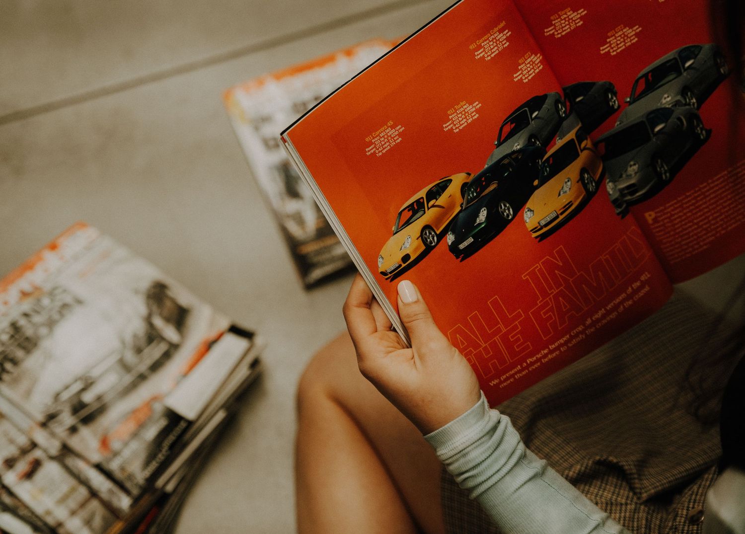 Someone holding an orange book while comic books or magazines are scattered on a beige surface.