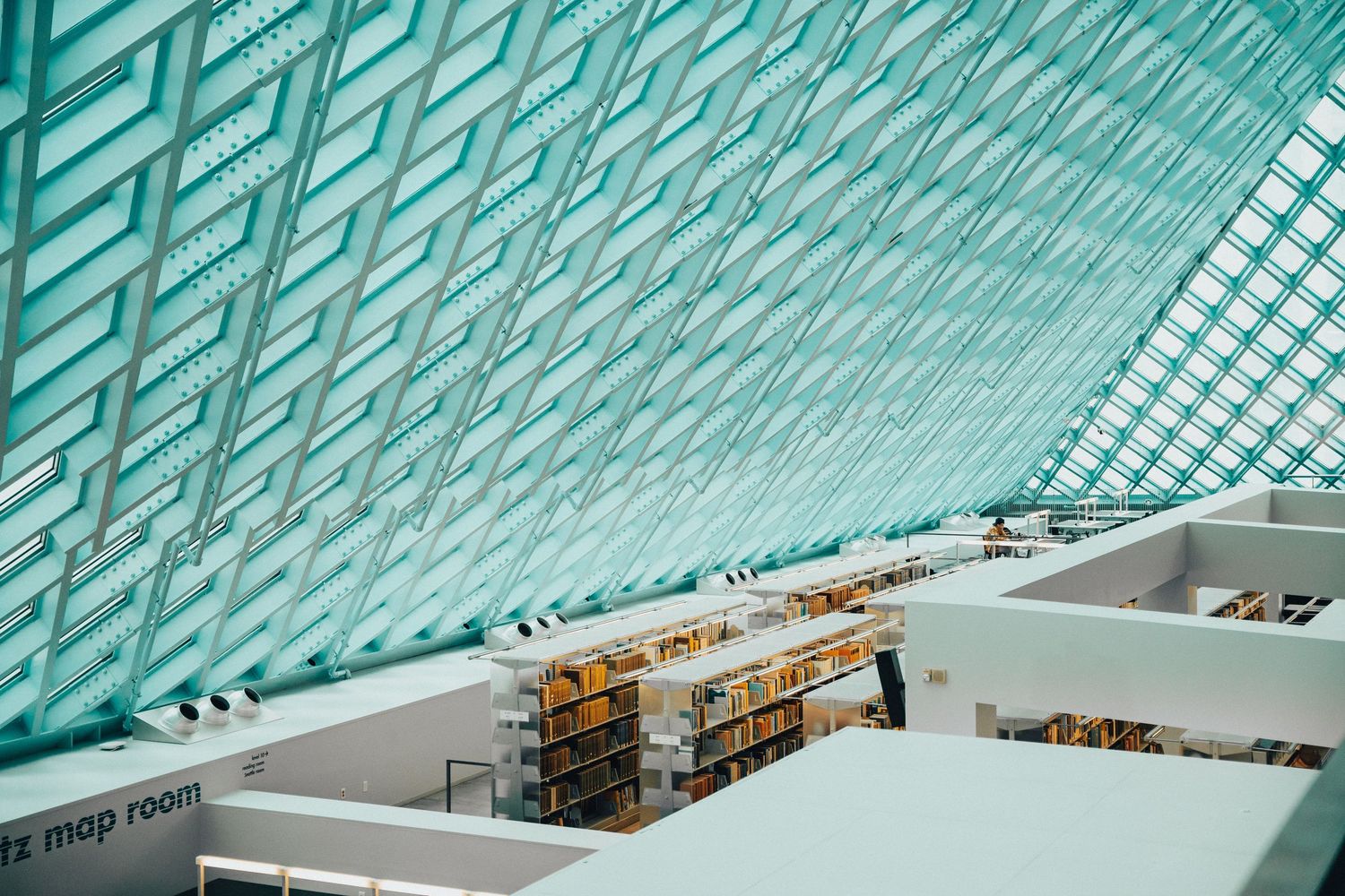 Interior of a modern public library with geometric glass ceiling and rows of bookshelves lit by natural light.