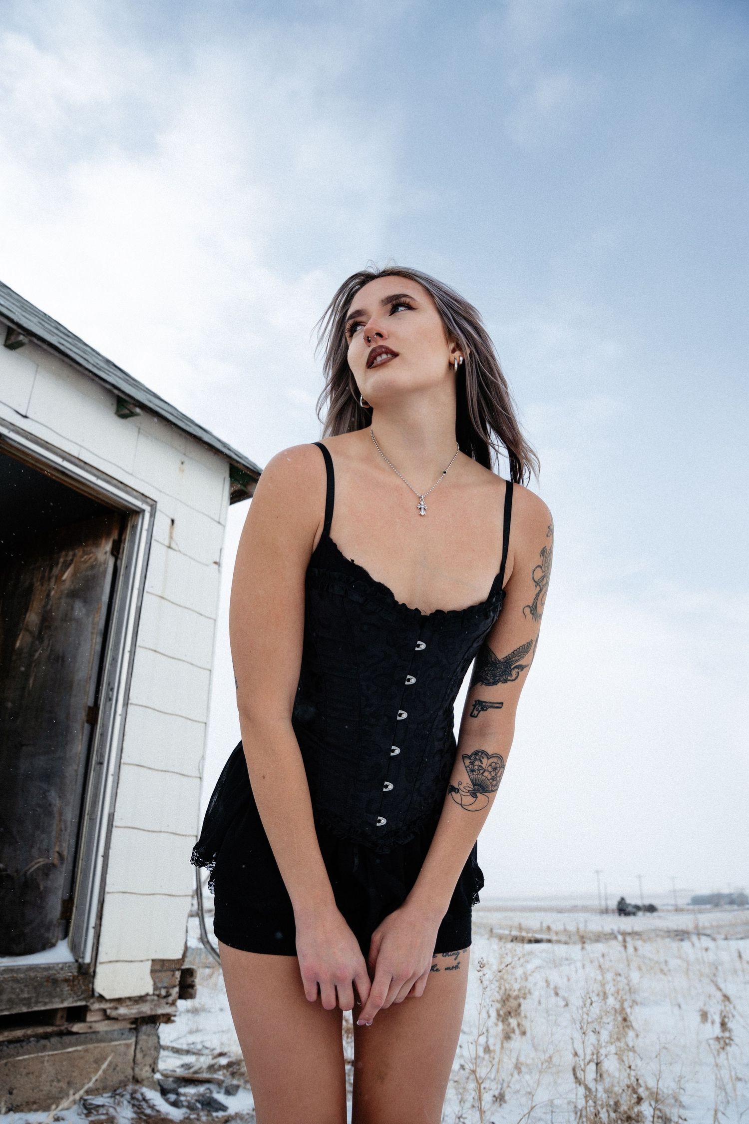 A person in a black corset top and shorts stands near a white building on a winter day.
