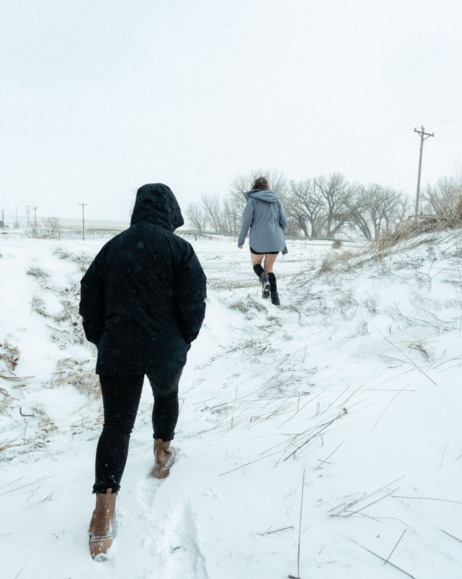 Two people hiking on a snowy trail during winter wearing boots and warm clothing on a hazy overcast day.