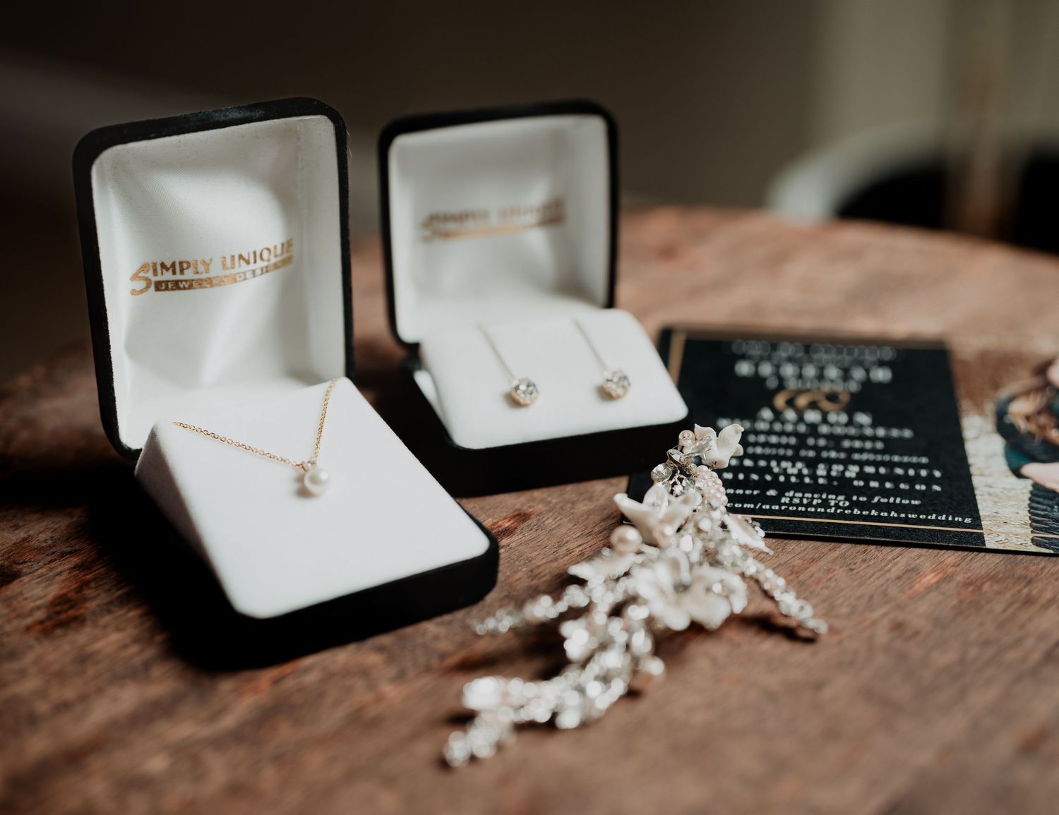 Wedding rings and delicate coral decorative pieces displayed in elegant black jewelry boxes against a warm wooden surface.
