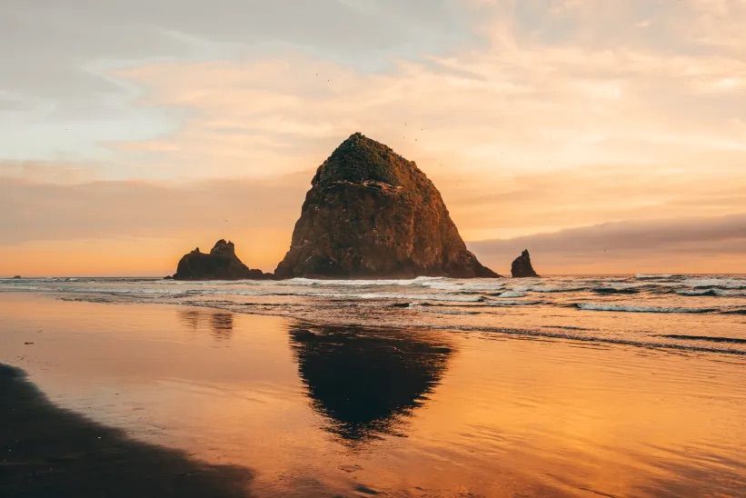 Haystack Rock reflects in wet sand during golden sunset at Cannon Beach, Oregon.