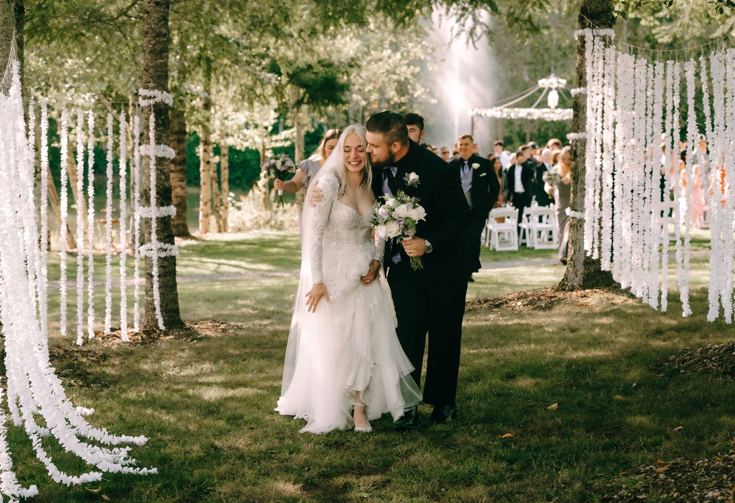 Romantic wedding exit through an aisle decorated with hanging white floral arrangements and string lights.