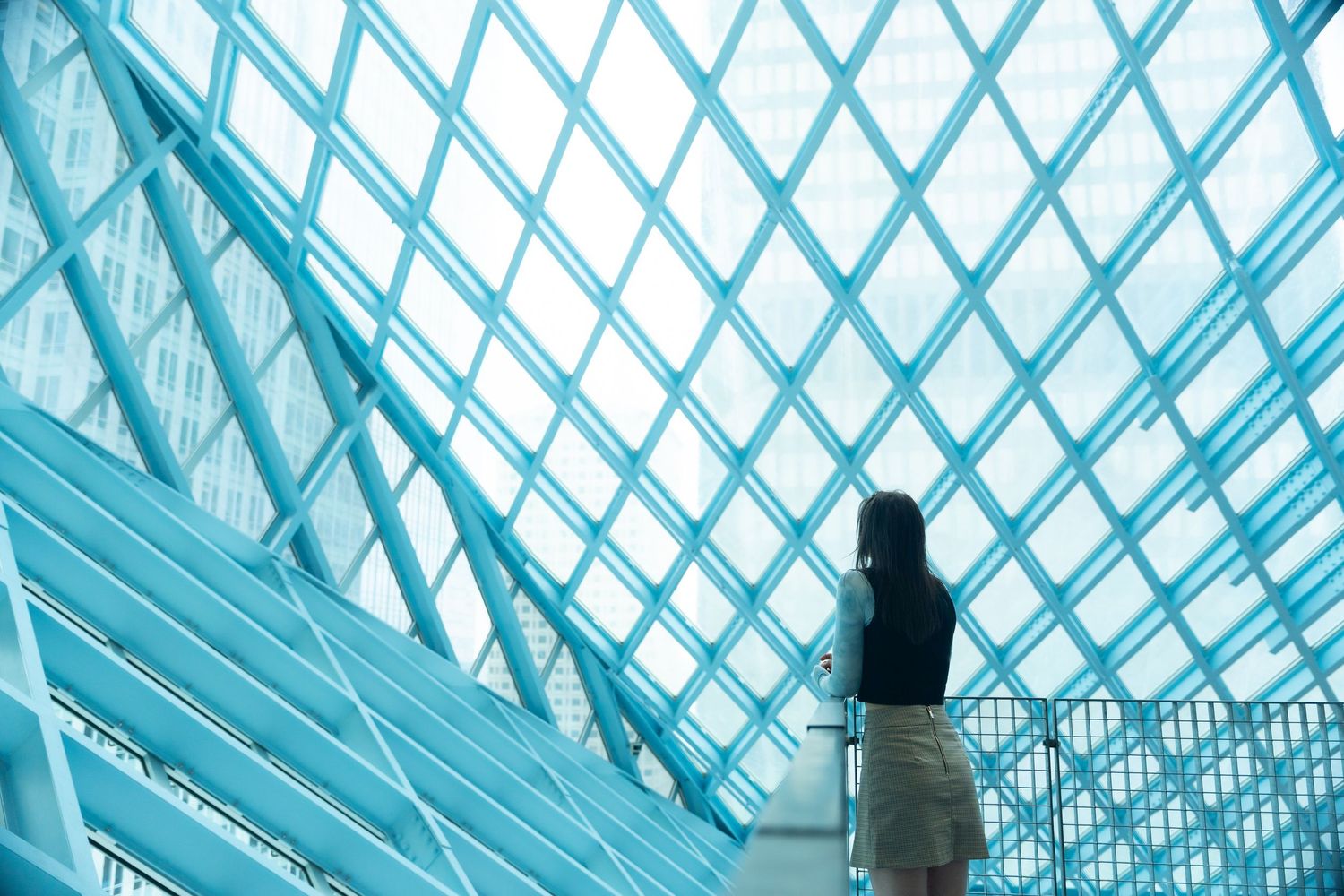 A silhouetted figure stands beneath a modern glass ceiling with geometric diamond patterns in turquoise lighting.