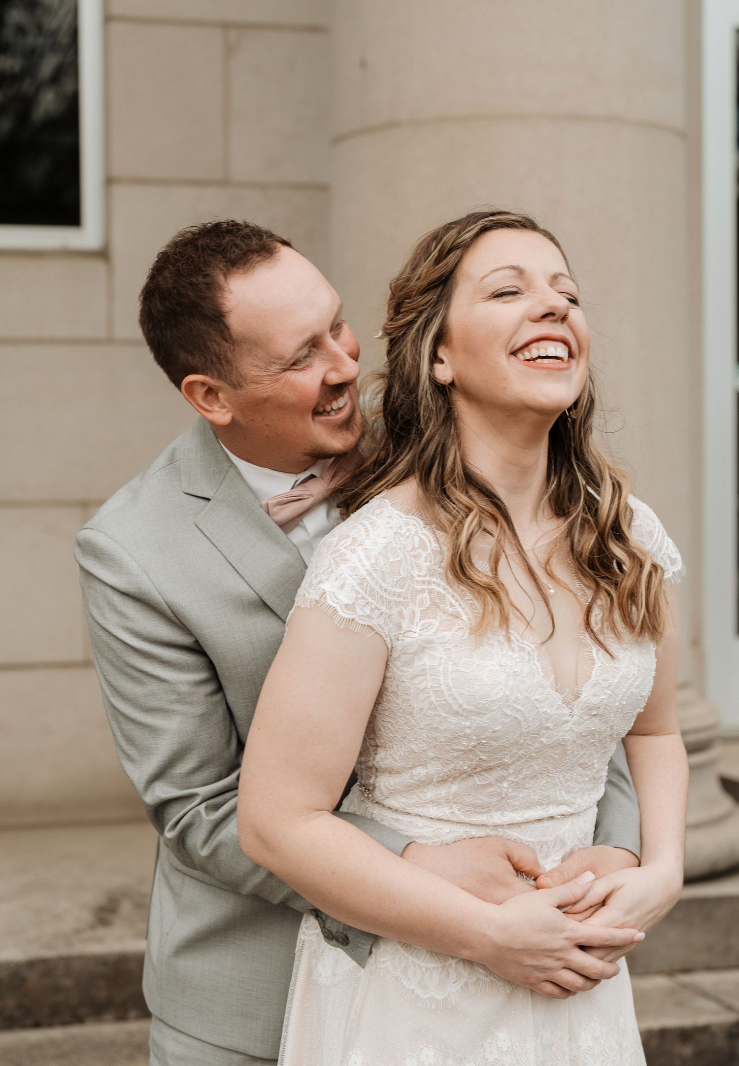 A couple laughs and embraces joyfully during their wedding portrait session in a light and airy setting.