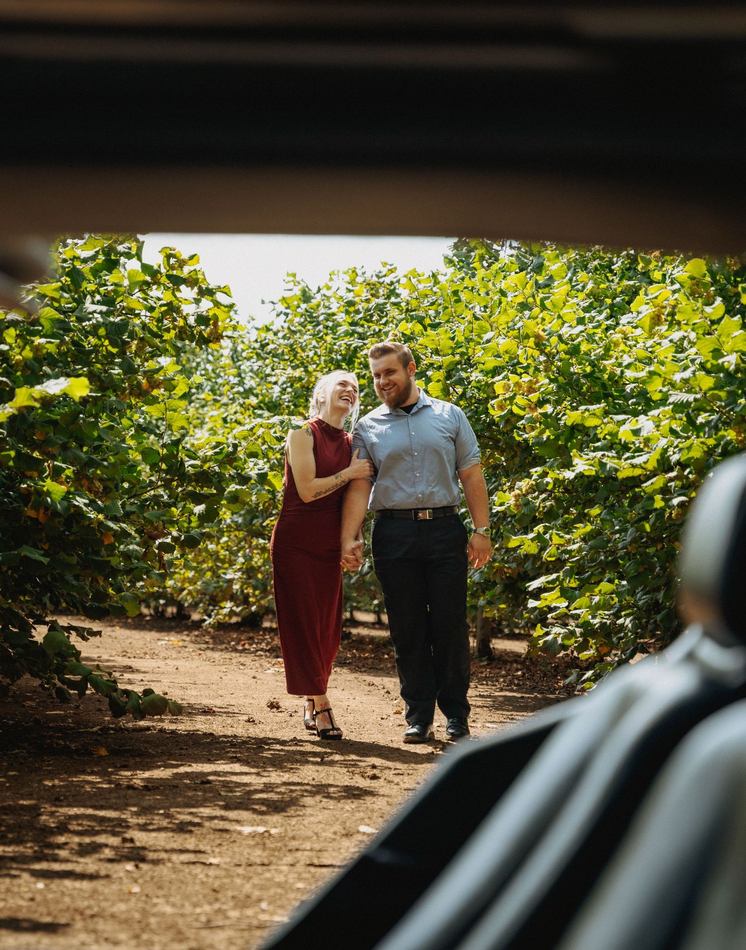Natural engagement portrait taken through car window on wooded path.