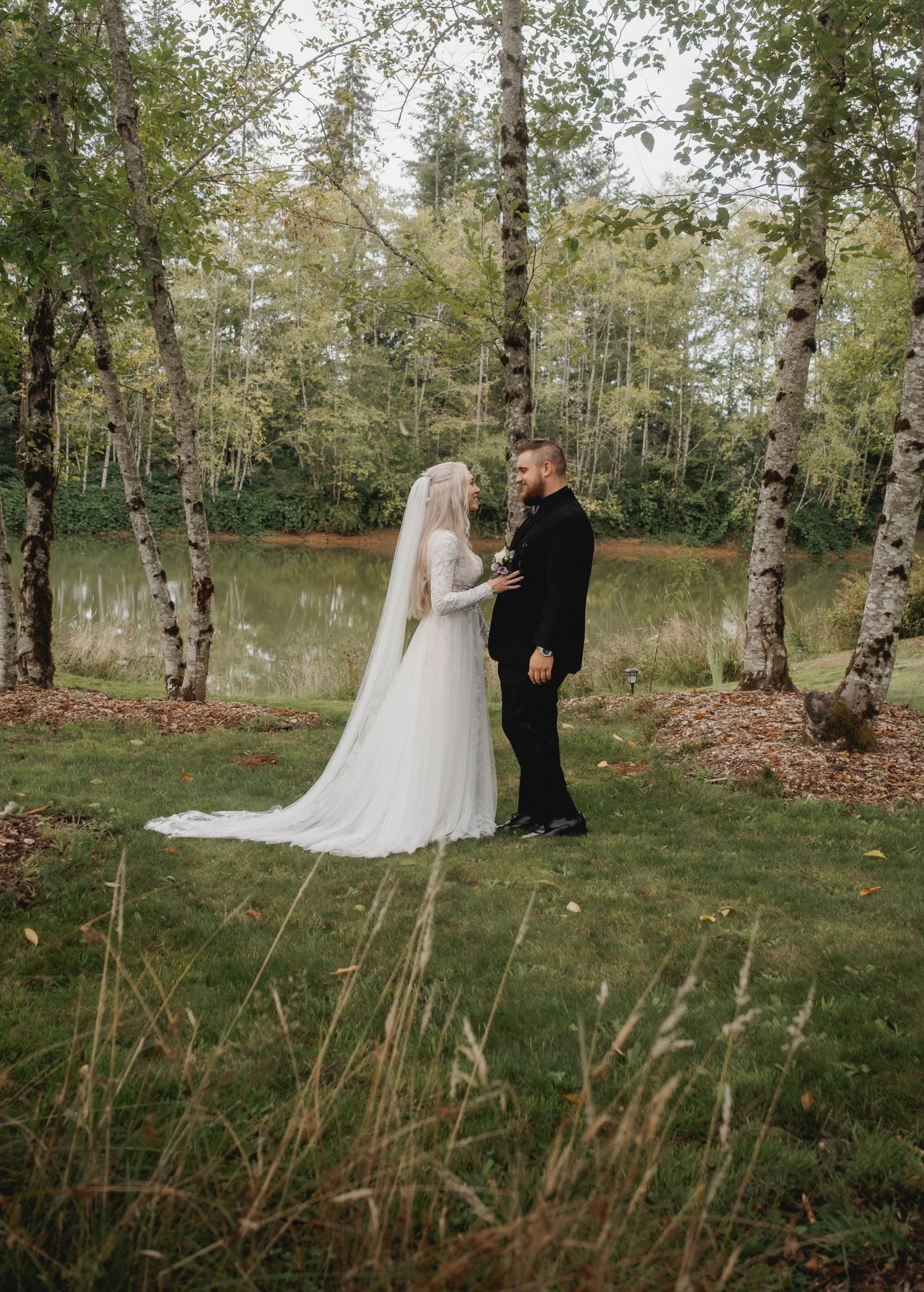 Full-length wedding portrait in a serene birch forest with tall grass and natural scenery.