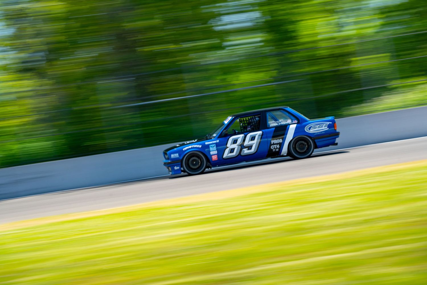 NASCAR race car speeds past green grass during a racing competition on a sunny day.