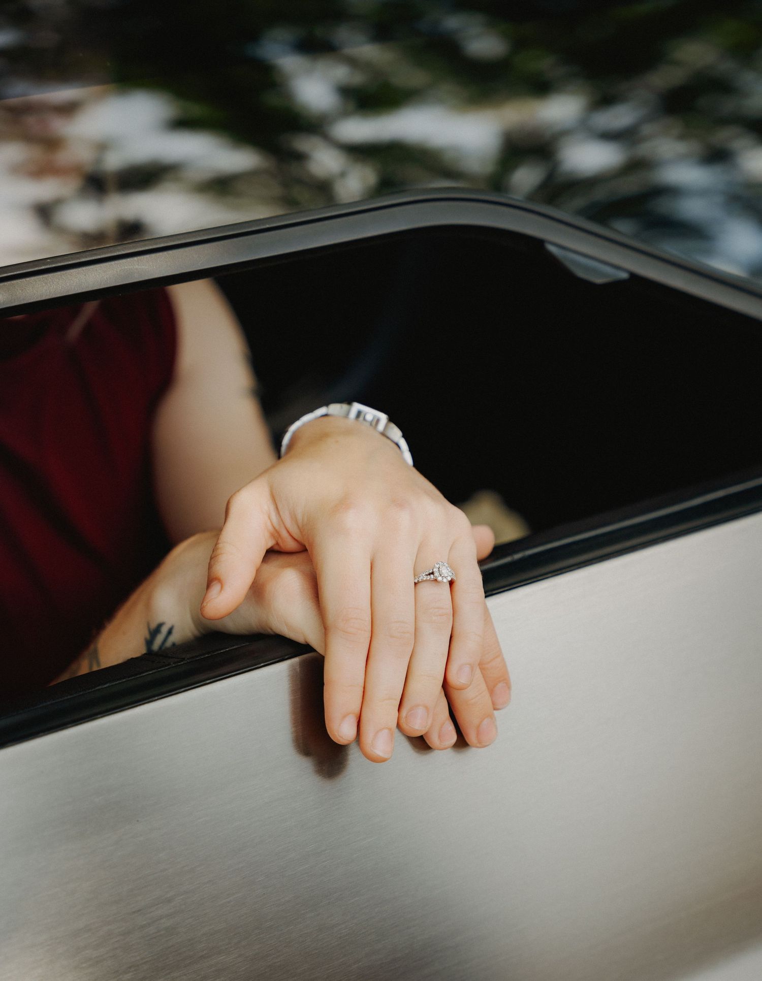 A close-up shot of hands wearing engagement rings resting on a car window.
