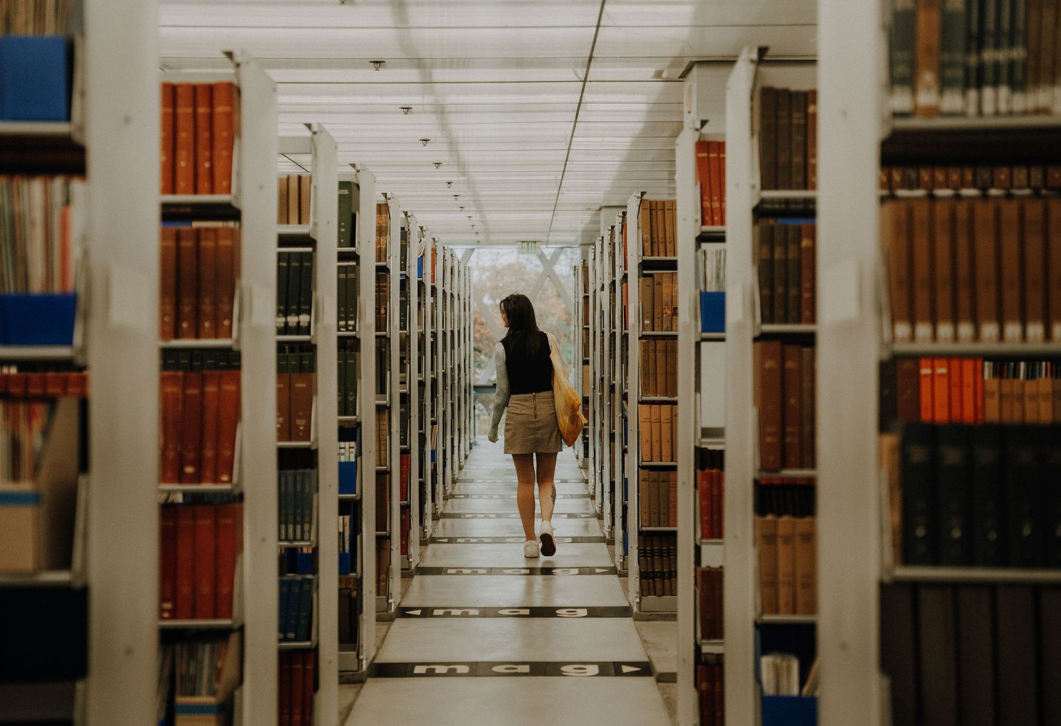 Long symmetrical library corridor lined with bookshelves and individuals studying between rows.