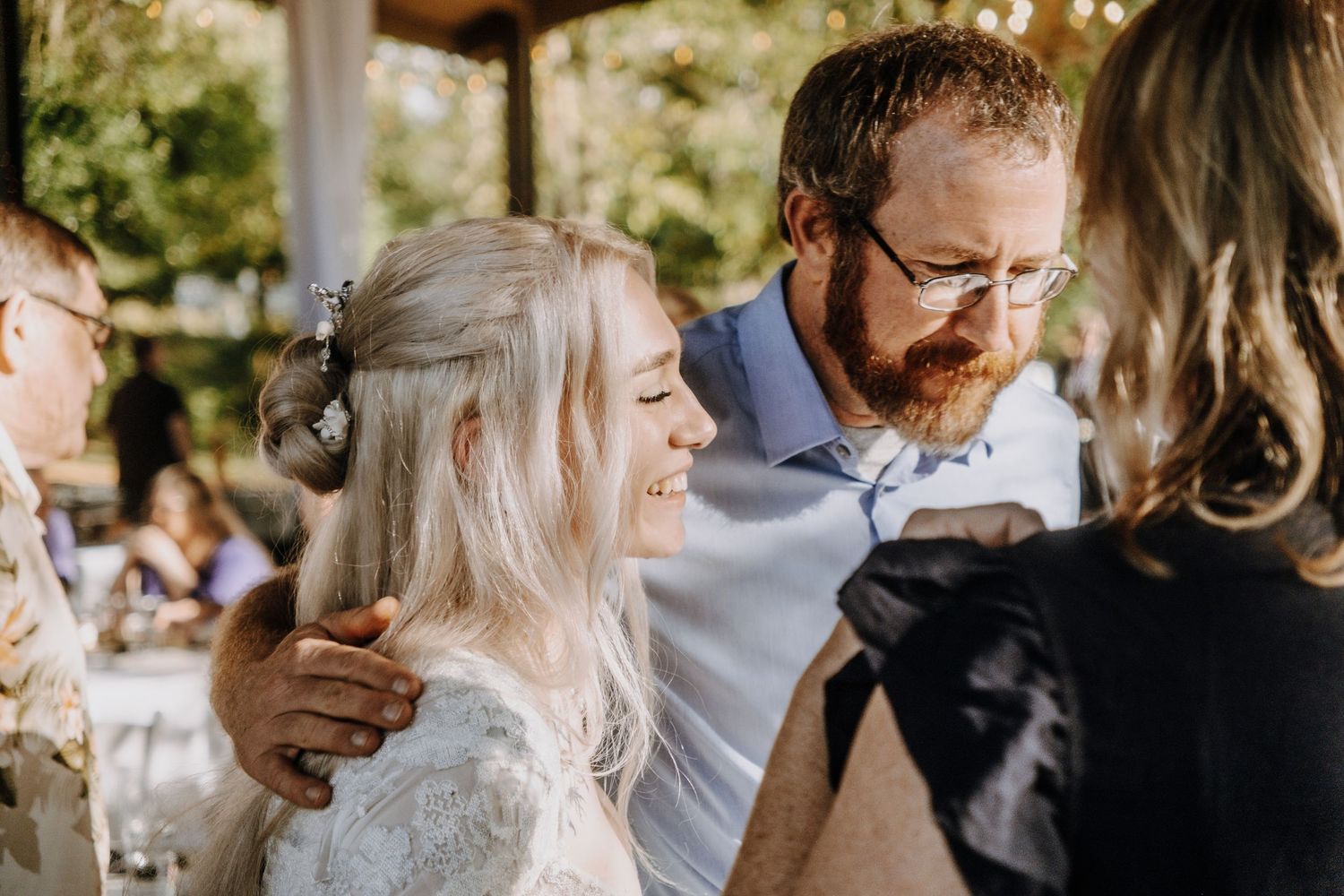 Wedding guests laugh and mingle during an outdoor celebration in warm sunlight.