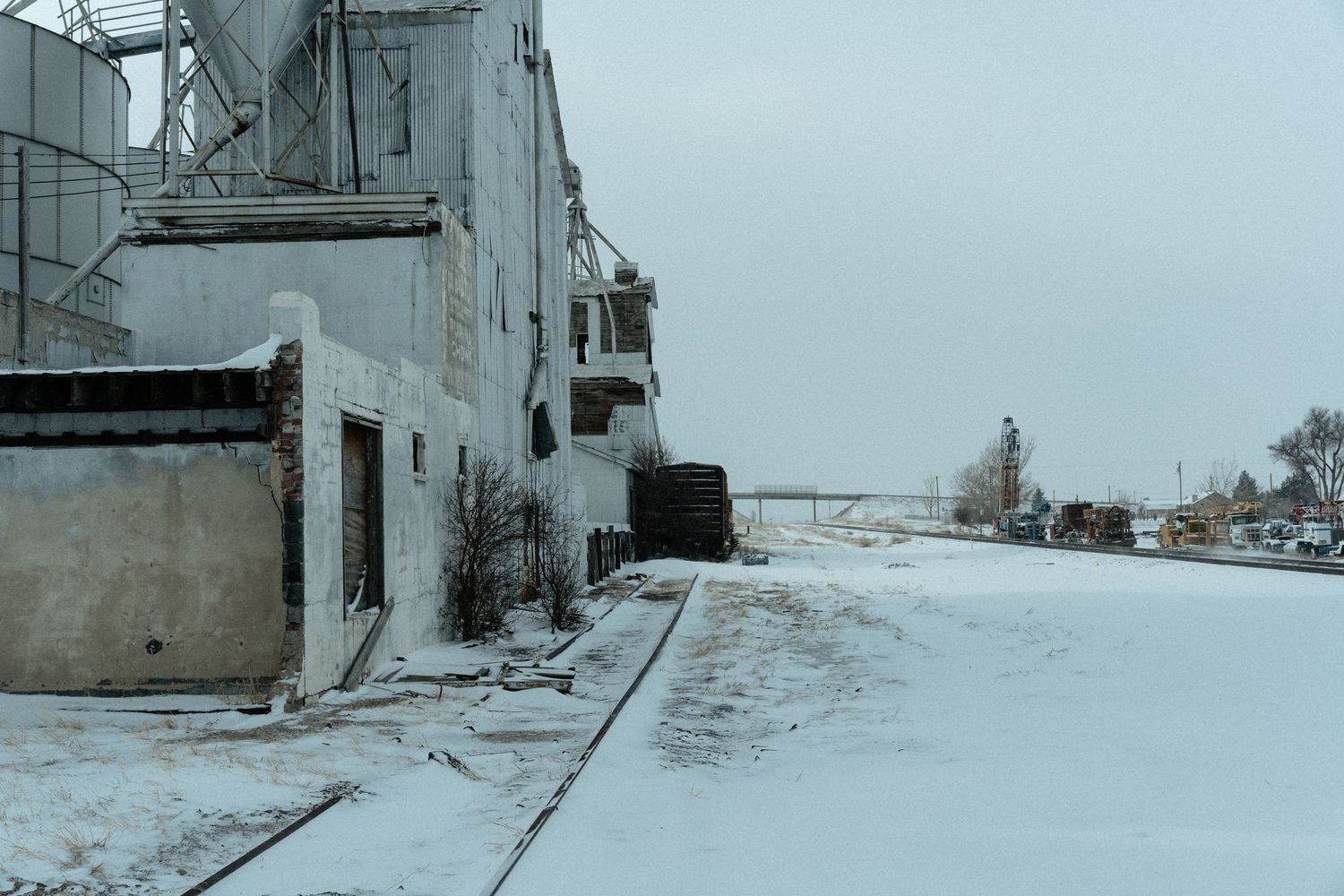 Snow covered industrial building exterior with gray concrete walls and metal structures in winter landscape.